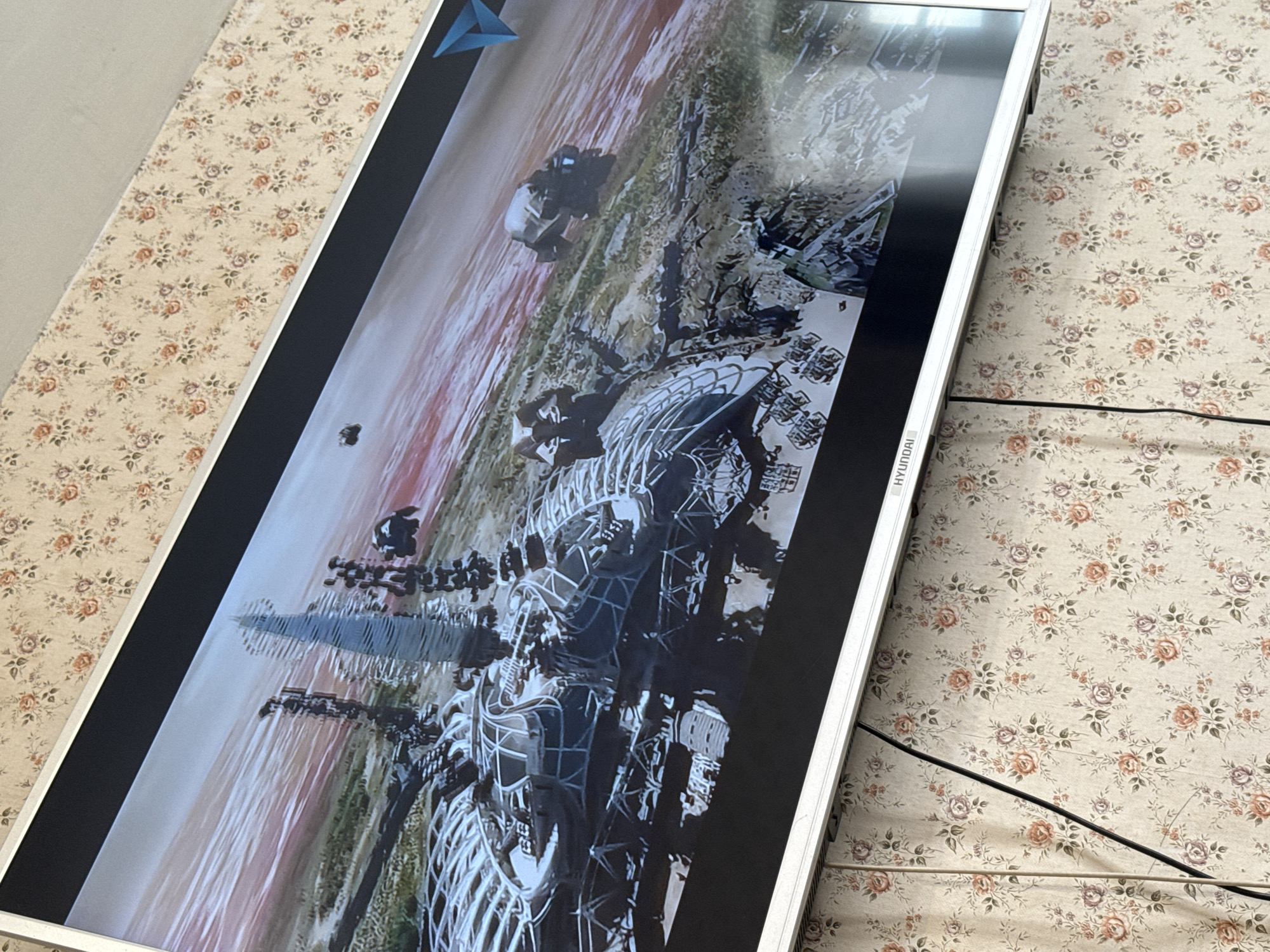 A Hyundai television displaying digital art is positioned on a surface with a floral patterned cover. The artwork features images suggesting landscapes with abstract, structural elements. The precise location within Mytishchi, Russia, is not identifiable from the provided visual data.