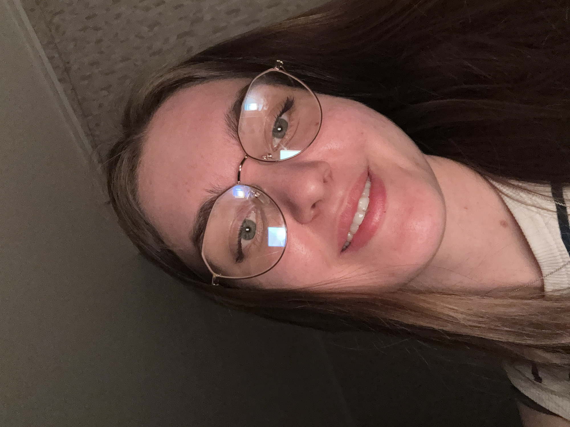 A selfie of a woman with light brown hair and fair skin, wearing gold-framed glasses, smiling slightly. The background appears to be a neutral gray wall. There is no information in the image to indicate that it was taken in Perm, Russia.