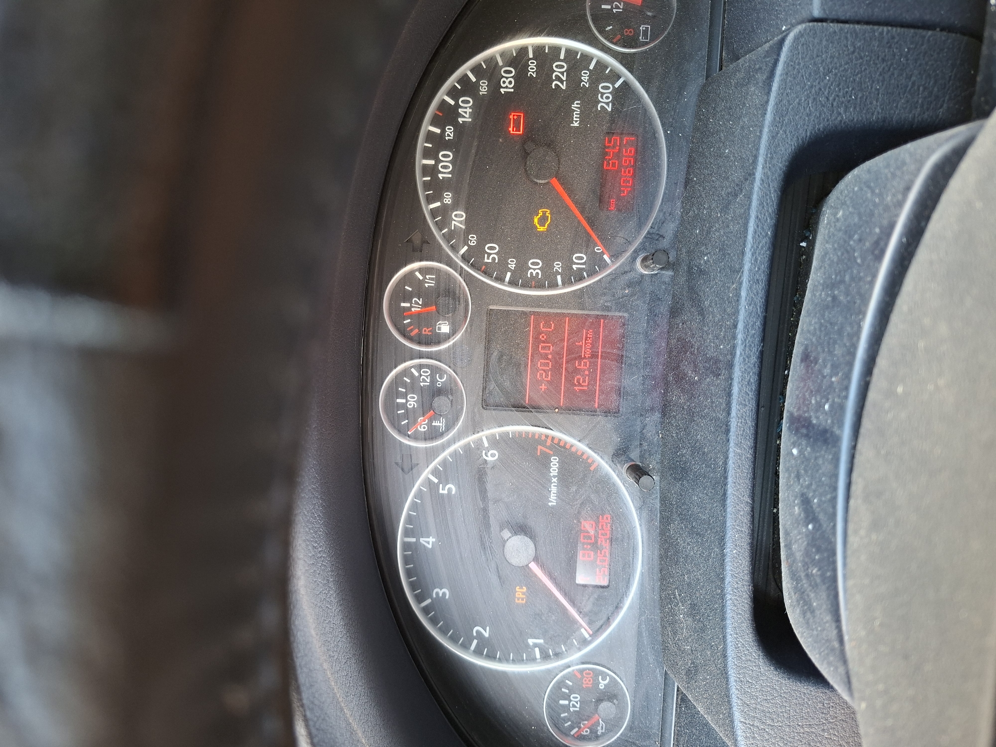 The image shows the dashboard of a car. The speedometer reads 64.5 km/h and the odometer displays 406967. Warning lights for the battery and engine are illuminated. The tachometer indicates around 0.8 (800 RPM). The date displayed is 25.05.2026. The temperature shown is 20 degrees Celsius. The image shows the engine light is on. There is no evidence within the image to indicate a location in the city of Plovdiv, Bulgaria.