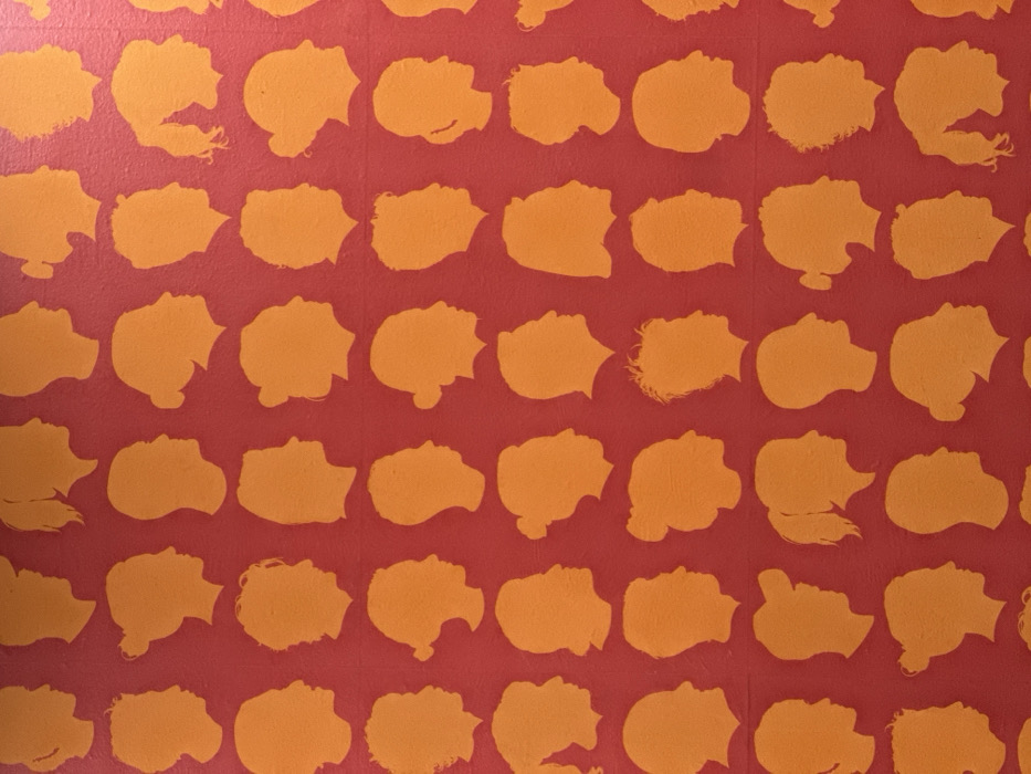A red background is patterned with rows of orange silhouettes of people's profiles. The profiles, mostly facing right, have varied hairstyles, some with long hair and some with short. The arrangement is grid-like, with each silhouette spaced evenly from the others. The texture of the background appears slightly rough or textured.