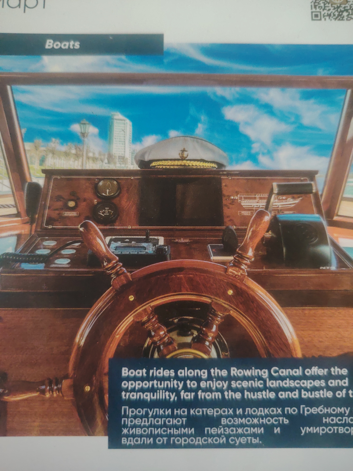 The image shows the interior of a boat, focusing on the captain's helm. A large wooden steering wheel is prominent in the foreground. Behind it, a polished wooden dashboard features various gauges, controls, and a radio. A white captain's hat with a gold braid band and an anchor emblem rests on the dashboard. The background depicts a bright blue sky with white clouds, and in the distance, a city skyline with buildings and palm trees. Text overlays on the image, partially in English and partially in Russian, advertise boat rides along the "Rowing Canal" offering "scenic landscapes and tranquility, far from the hustle and bustle of the city." The image does not contain any information about the city of Bahshitpa, Uzbekistan.
