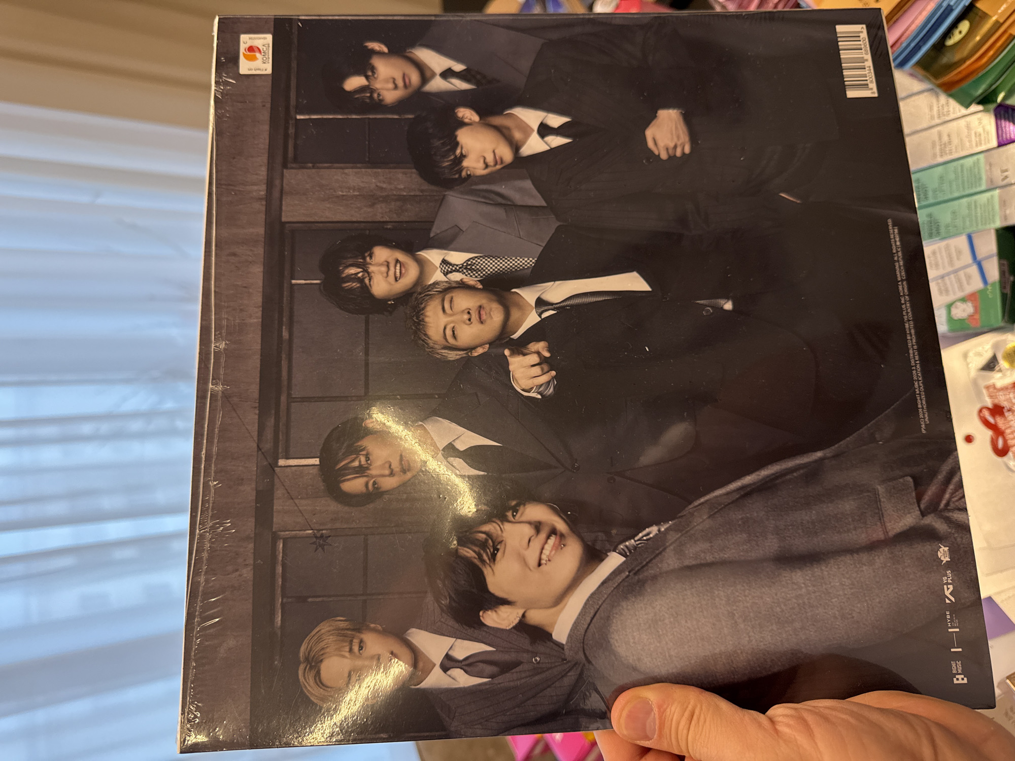 The image shows a person holding a vinyl record album featuring the South Korean boy band BTS. The album cover is a black and white photo of the seven members of the band in suits. The album is in its original plastic wrapping. The location of the image is not specified and no information is available to support the location being in Krasnoyarsk, Russia.