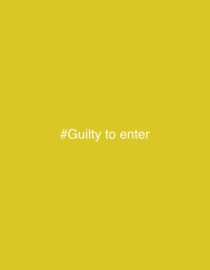 The image displays a plain, solid mustard yellow background. Centered on this background is text in a light gray or off-white color. The text reads "#Guilty to enter". No other subjects, objects, or specific scenes are visible in the image. There are no discernible activities, time of day, weather conditions, or emotional expressions depicted. The image provides no visual cues regarding its location, though its context is Chaikovsky, Russia.
