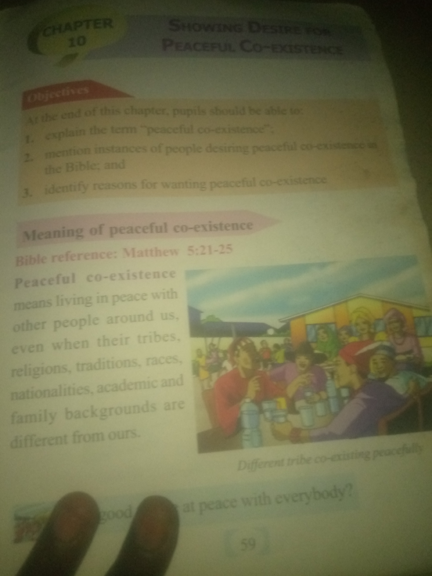 The image is a photograph of an open textbook page. The page is divided into sections with headings such as "CHAPTER 10" and "Objectives." Below "Objectives" are numbered points related to explaining the term "peaceful co-existence" and mentioning instances of people desiring peaceful co-existence.
A prominent section titled "Meaning of peaceful co-existence" is present, followed by a Bible reference: "Matthew 5:21-25." The text defines peaceful co-existence as "means living in peace with other people around us, even when their tribes, religions, traditions, races, nationalities, academic and family backgrounds are different from ours."
To the right of this text is an illustration depicting a group of people, seemingly diverse in age and appearance, gathered around tables outside a building. The illustration shows individuals holding cups and bottles, suggesting a communal gathering. The sky in the illustration is a bright blue.
Below the main text and illustration, a caption reads "Different tribe co-existing peacefully." Further down the page, a question is posed: "good at peace with everybody?" and the page number "59" is visible at the bottom right.
The image also shows portions of two fingers in the foreground, partially obscuring the bottom left corner of the textbook page. The overall lighting suggests it was taken indoors under artificial light. There is no visual information in the image that would indicate the location in the city of Jauro Yinu, Nigeria.