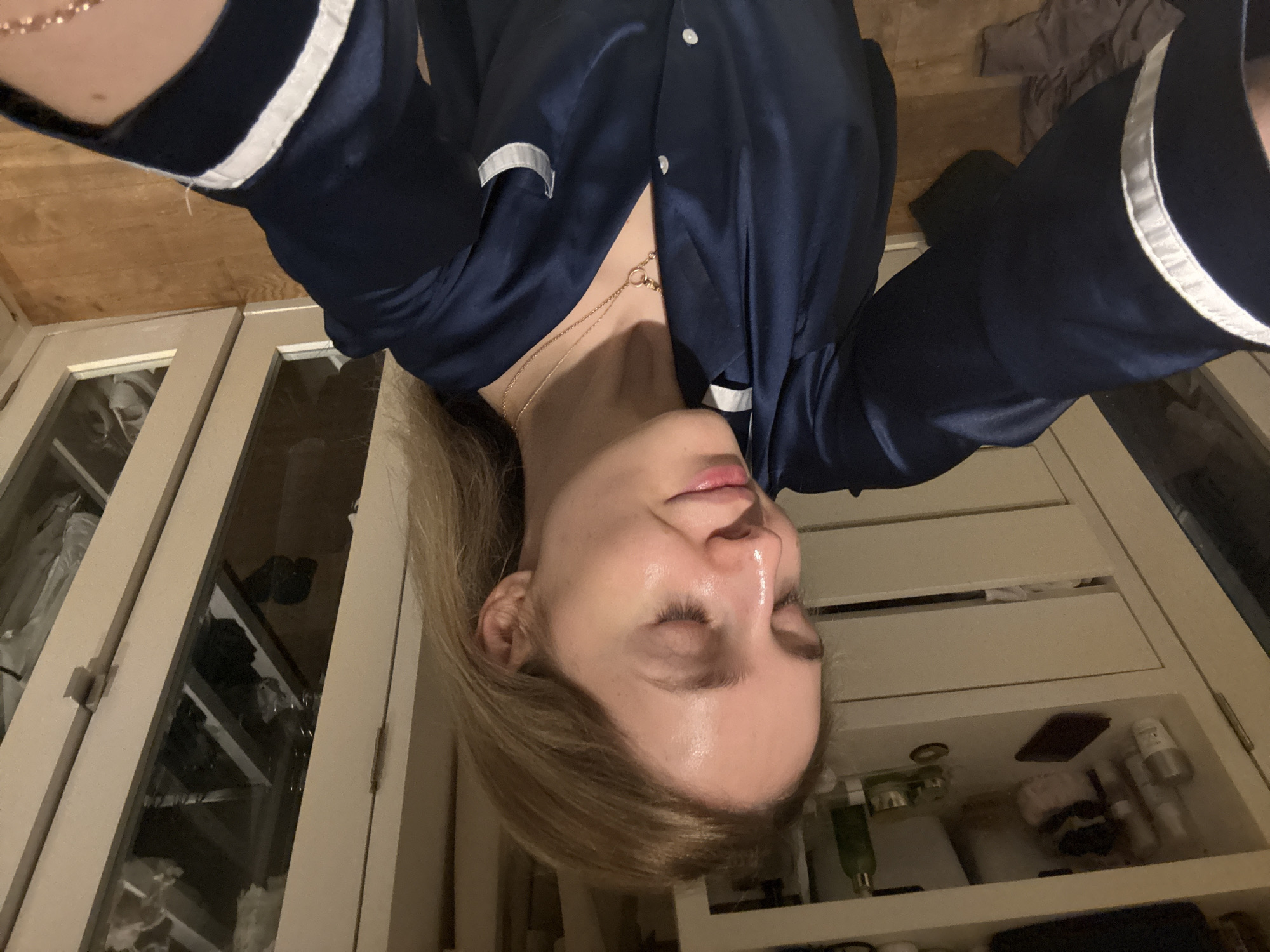 A person is upside down in front of a cabinet. The person is wearing a dark blue shirt with white trim. The cabinet is white and has various items inside. The environment appears to be inside a home. There is no evidence to suggest a location within Mexico City.
