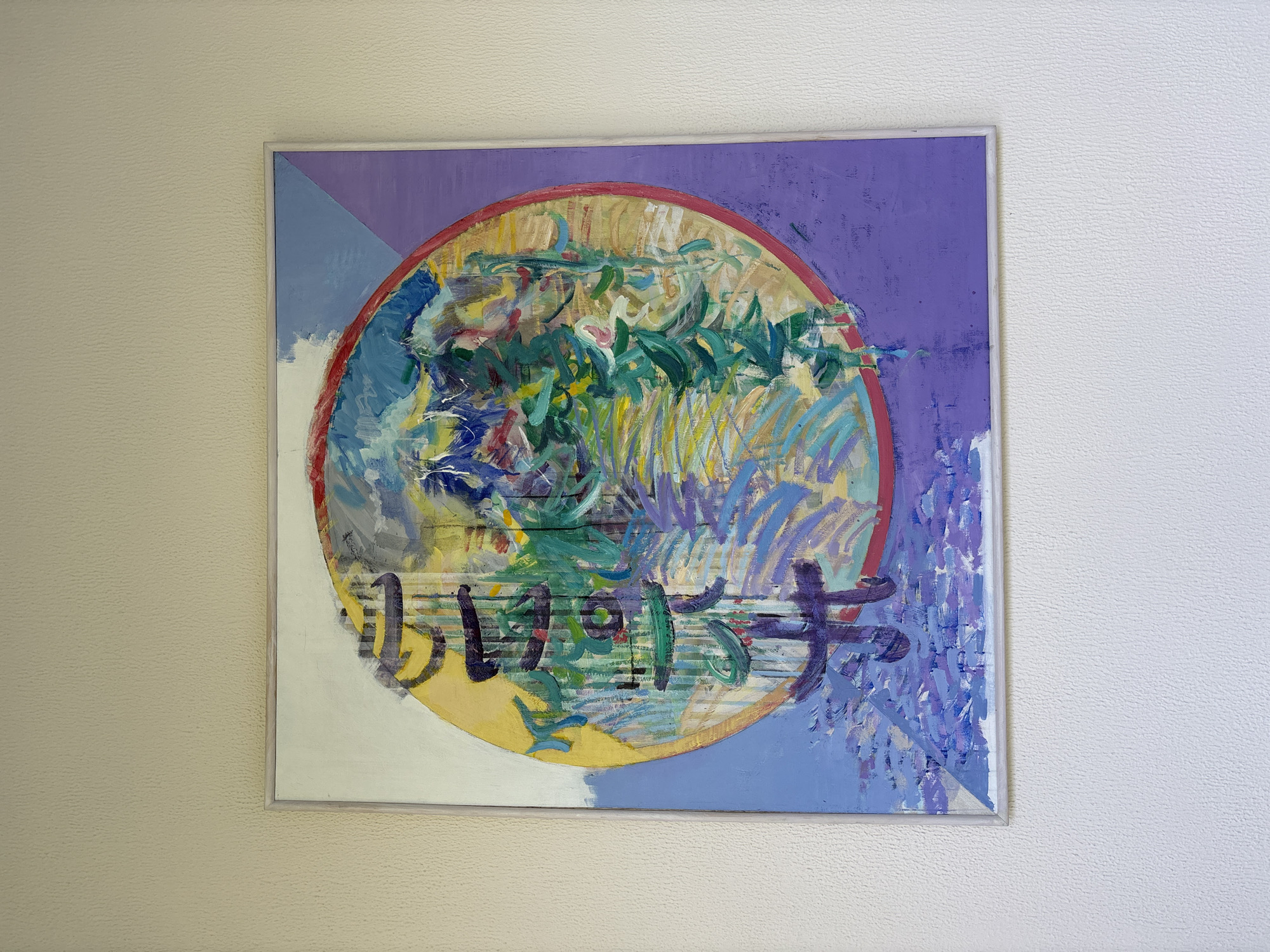 The image shows a framed abstract painting hanging on a textured, light-colored wall. The painting is predominantly circular with a red border, filled with vibrant and varied brushstrokes of blue, yellow, green, purple, and white. There are vertical elements resembling bamboo or reeds within the circle, and some darker, stylized characters that appear to be calligraphy. The background of the painting consists of diagonal planes of purple and light blue. The wall the painting is on is a neutral, textured surface. This scene is located in the hallway of a modern building. It is unclear if this is Varna, Bulgaria.