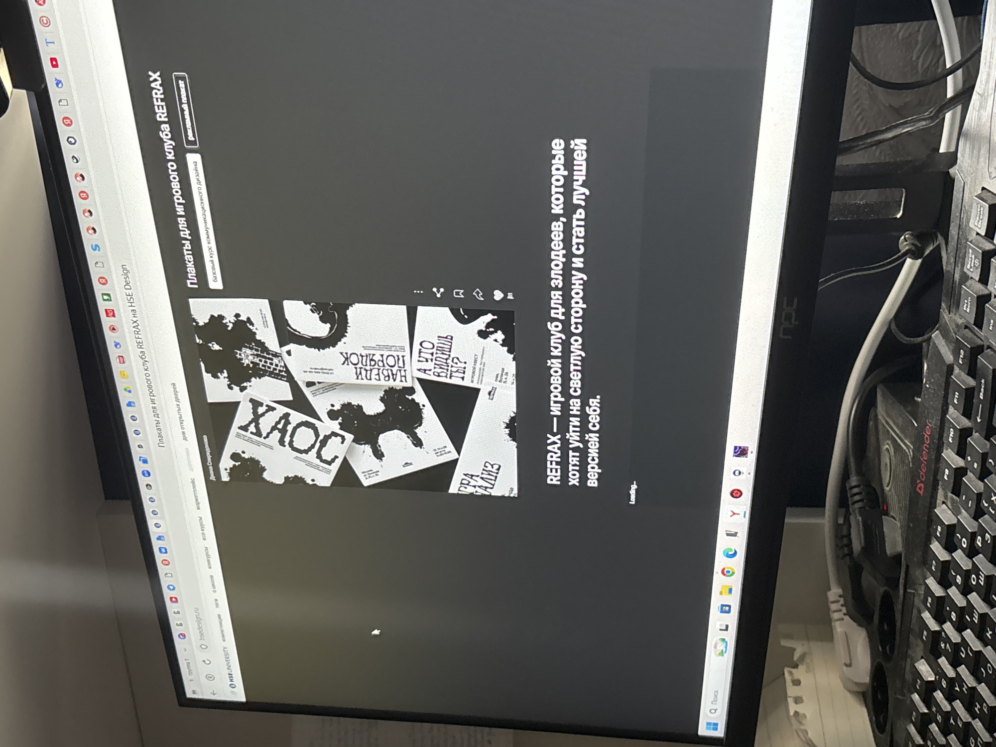 An indoor, slightly angled shot captures a computer monitor displaying a website, with a black keyboard and various cables visible to the right. The monitor shows a webpage from "hsedesign.su," likely a portfolio or project page associated with HSE University in Moscow, Russia.
The main content on the screen is titled "Плакаты для игрового клуба REFRAX на HSE Design" (Posters for REFRAX gaming club at HSE Design). Below this, a section is labeled "Базовый курс коммуникационного дизайна" (Basic course in communication design) and "рекламный плакат" (promotional poster). Several graphic design posters are partially visible, featuring bold Russian text such as "XAOC" (Chaos), "НАВЕДИ ПОРЯДОК" (Bring Order), and "А ЧТО ВИДИШЬ ТЫ?" (What do you see?), along with illustrative elements. Another poster mentions "ИГРОВОЙ КВЕСТ" (Game Quest) and "Воланда" (Voland).
A prominent text block on the right side of the screen reads: "REFRAX — игровой клуб для злодеев, которые хотят уйти на светлую сторону и стать лучшей версией себя." (REFRAX - a gaming club for villains who want to go over to the light side and become the best version of themselves.) A "Loading..." indicator is visible below this text. The browser's address bar confirms "hsedesign.su" and shows navigation links like "конкурсы" (contests), "все курсы" (all courses), and "дни открытых дверей" (open days).
To the right of the monitor, a black "D'defender" brand keyboard is present, along with a tangle of white and black cables, suggesting a desktop computer setup. A power strip is partially visible beneath the keyboard. The setting appears to be a workspace, likely in Moscow, given the Russian language and university context.