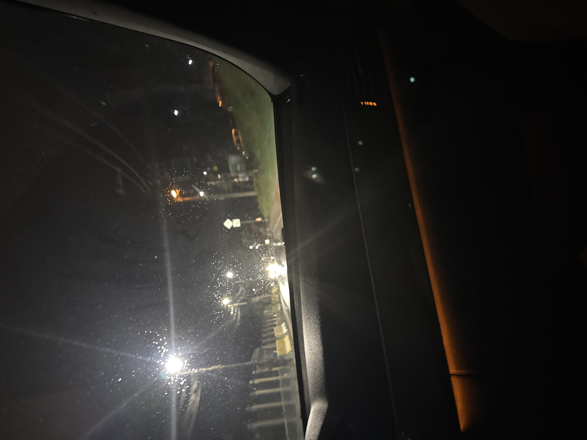 The image shows a view from inside a vehicle at night. Through the window, there is a view of what appears to be a pedestrian overpass or elevated walkway. The walkway consists of a series of steps leading up to a platform, and it is illuminated by streetlights. The vehicle's window is wet with raindrops. The setting appears to be urban, with street lighting visible. The location is likely Sofia, Bulgaria based on the image context.