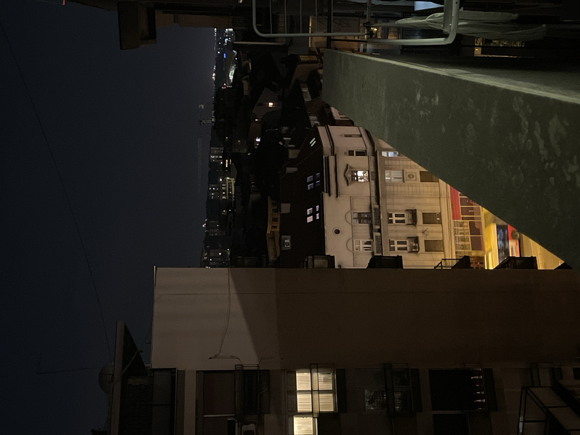 Nighttime rooftop view of Vracar, Belgrade, Serbia. Predominantly buildings with lit windows are visible. The sky is dark. A railing and roof edge are in the foreground.