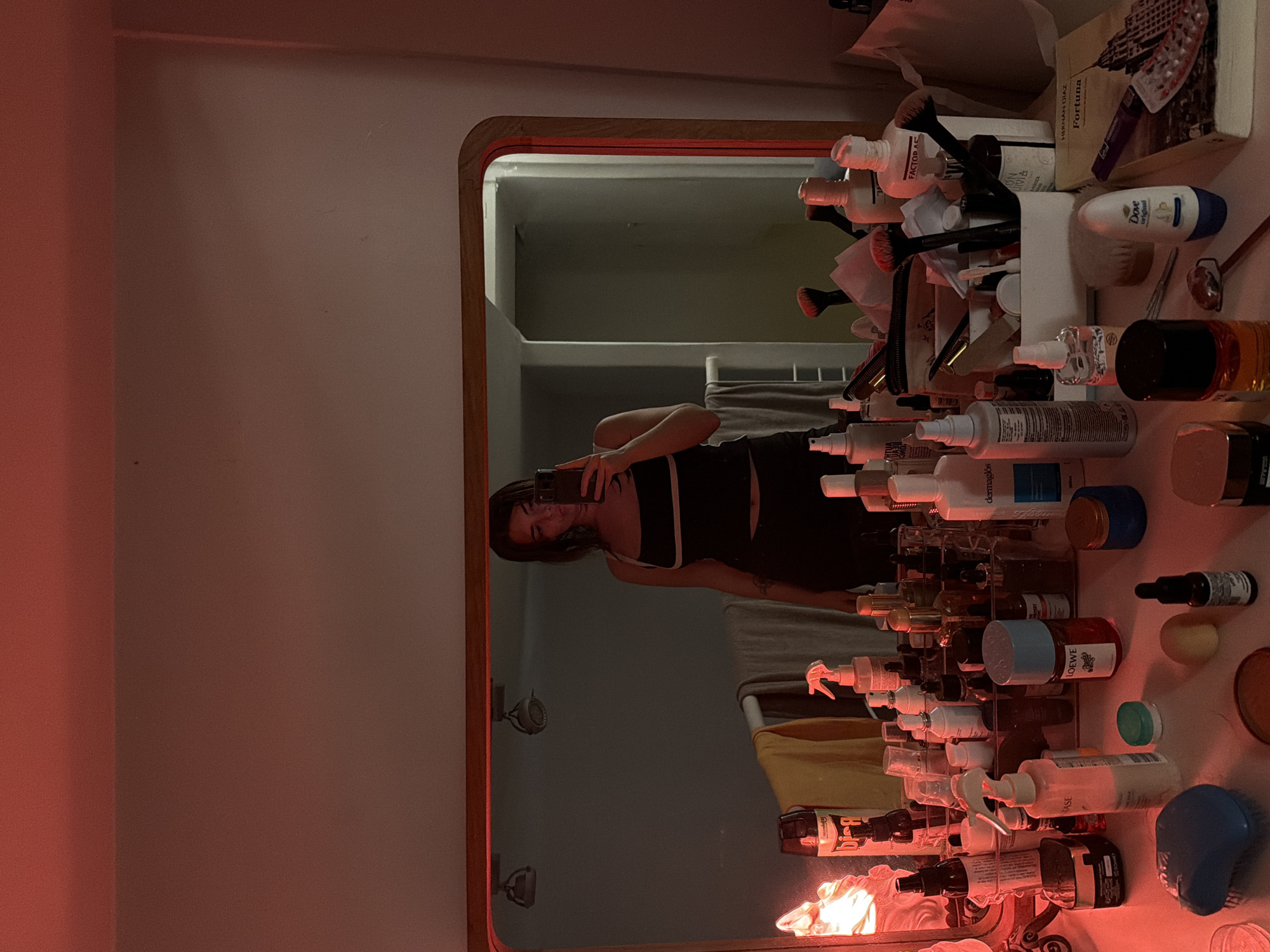 A person is reflected in a mirror surrounded by toiletries. The person is holding a phone to take a picture. The mirror is on a wall. It's impossible to determine from the image where this is located within the city of Buenos Aires, Argentina.