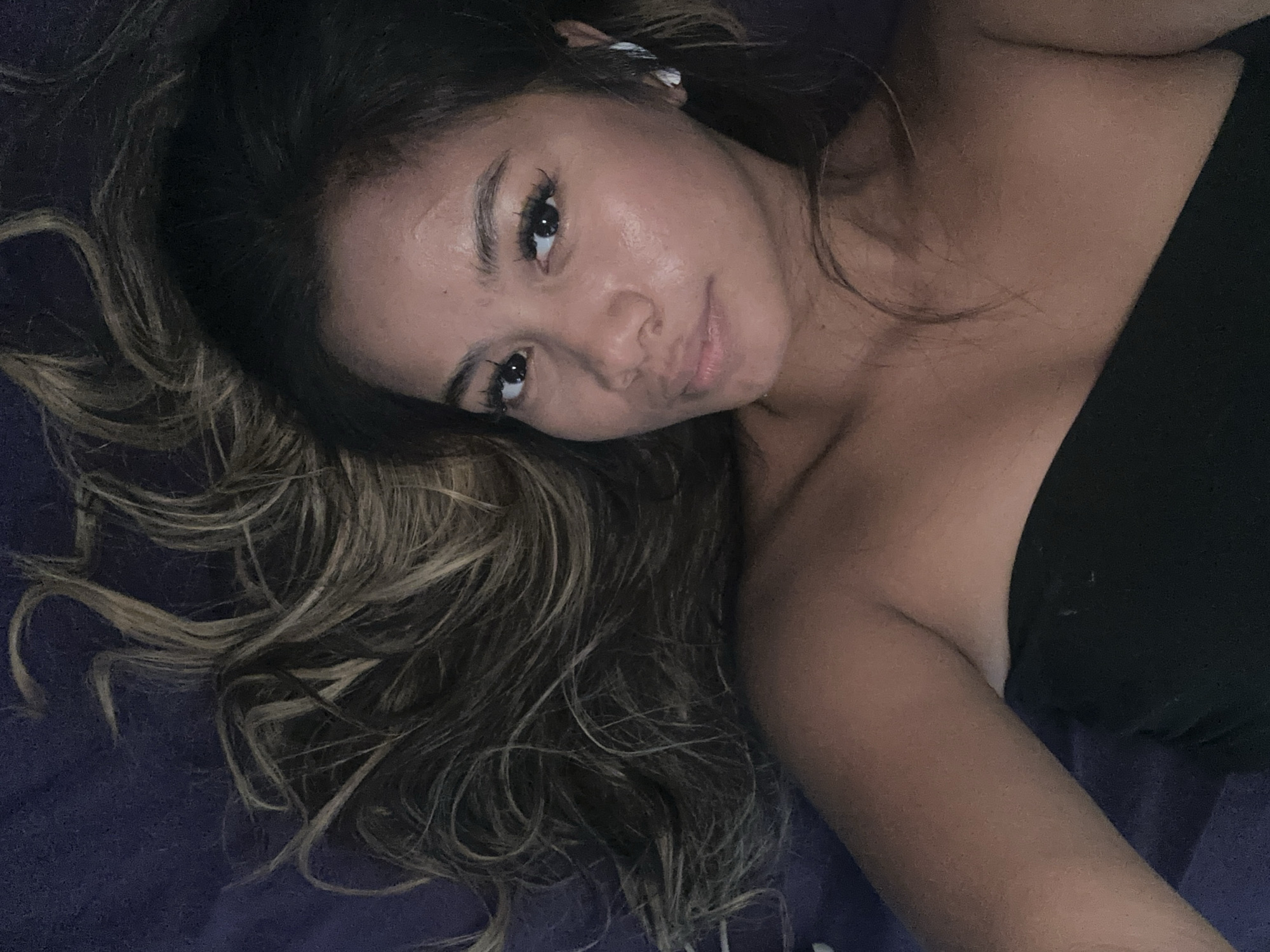 A person with tan skin and long, wavy hair is lying down. The hair, which is a mix of dark brown and blonde, is spread out to the left of the person's face. The person is wearing a black strapless top. The background appears to be a dark blue or purple surface.
The image does not contain information about location of North Jakarta, Indonesia.