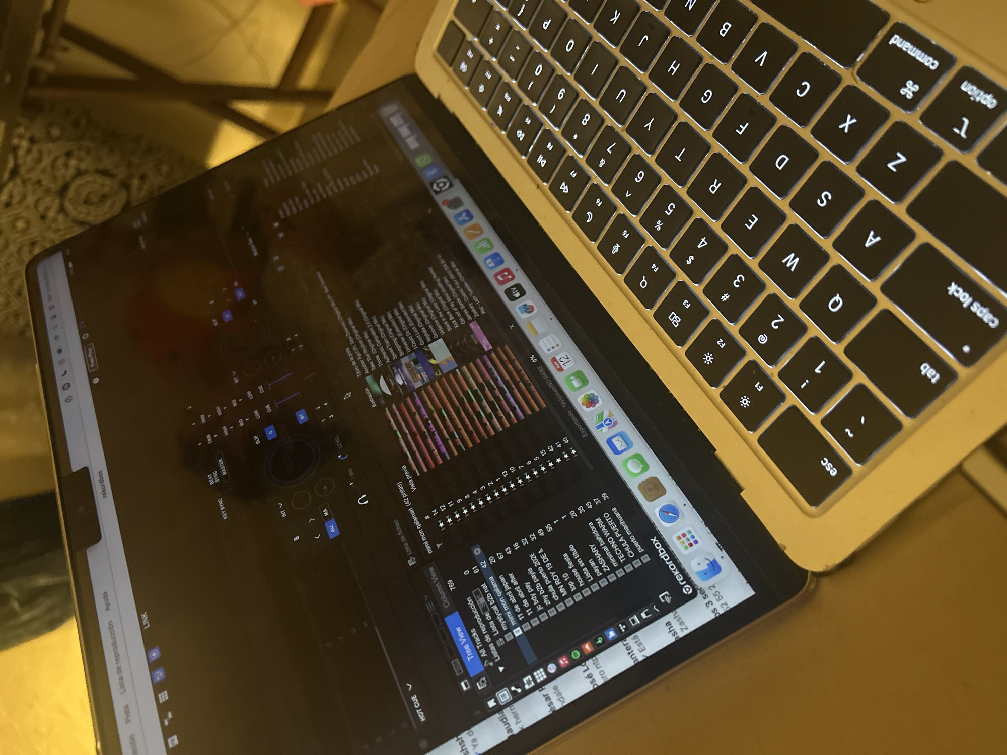 A tan-colored Macbook is open, displaying the Rekordbox software on its screen. The software shows a playlist with song titles and an audio mixing interface. The laptop is sitting on a table. The environment suggests an indoor setting, possibly a home or office. The location is unknown, and there is no evidence to suggest this is in Mexico City, Mexico.