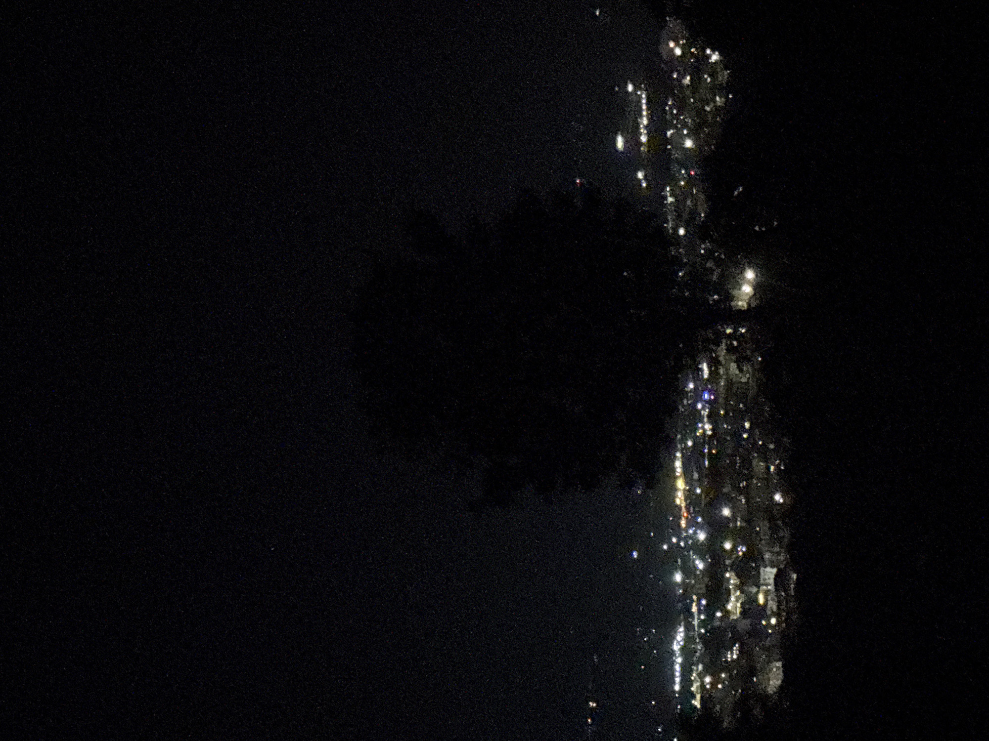 The image shows a night scene, likely in or near Marulevo, Bulgaria, with a dark sky. The right side of the image contains a vertical reflection of lights on a body of water, possibly a river or lake. These lights could originate from buildings or street lamps in Marulevo, but the details are obscured due to the darkness and reflection. The left portion of the image is mostly dark, suggesting open space or a less illuminated area. Due to the image quality, no people, subjects, or objects beyond the lights and water can be discerned.