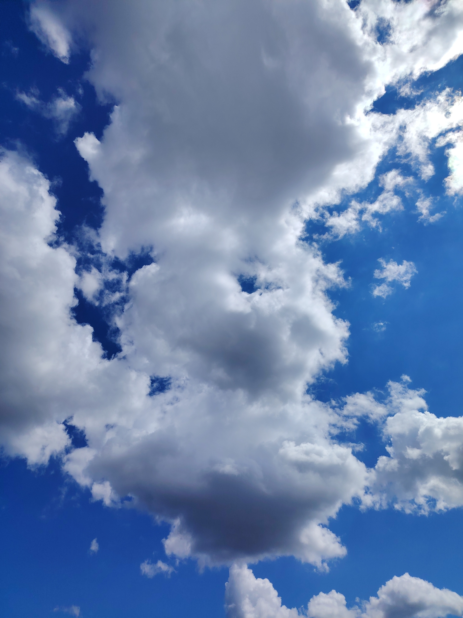 The image shows a bright blue sky with numerous white and gray cumulus clouds. The clouds vary in size and shape, some appearing puffy and rounded, while others are more spread out and wispy. Some portions of the clouds are casting shadows, suggesting a sunny day. The location is specified as the city of Chaikovsky, Russia, though this cannot be verified visually from the image. No people, subjects, objects, actions, or interactions are visible other than the sky and clouds.