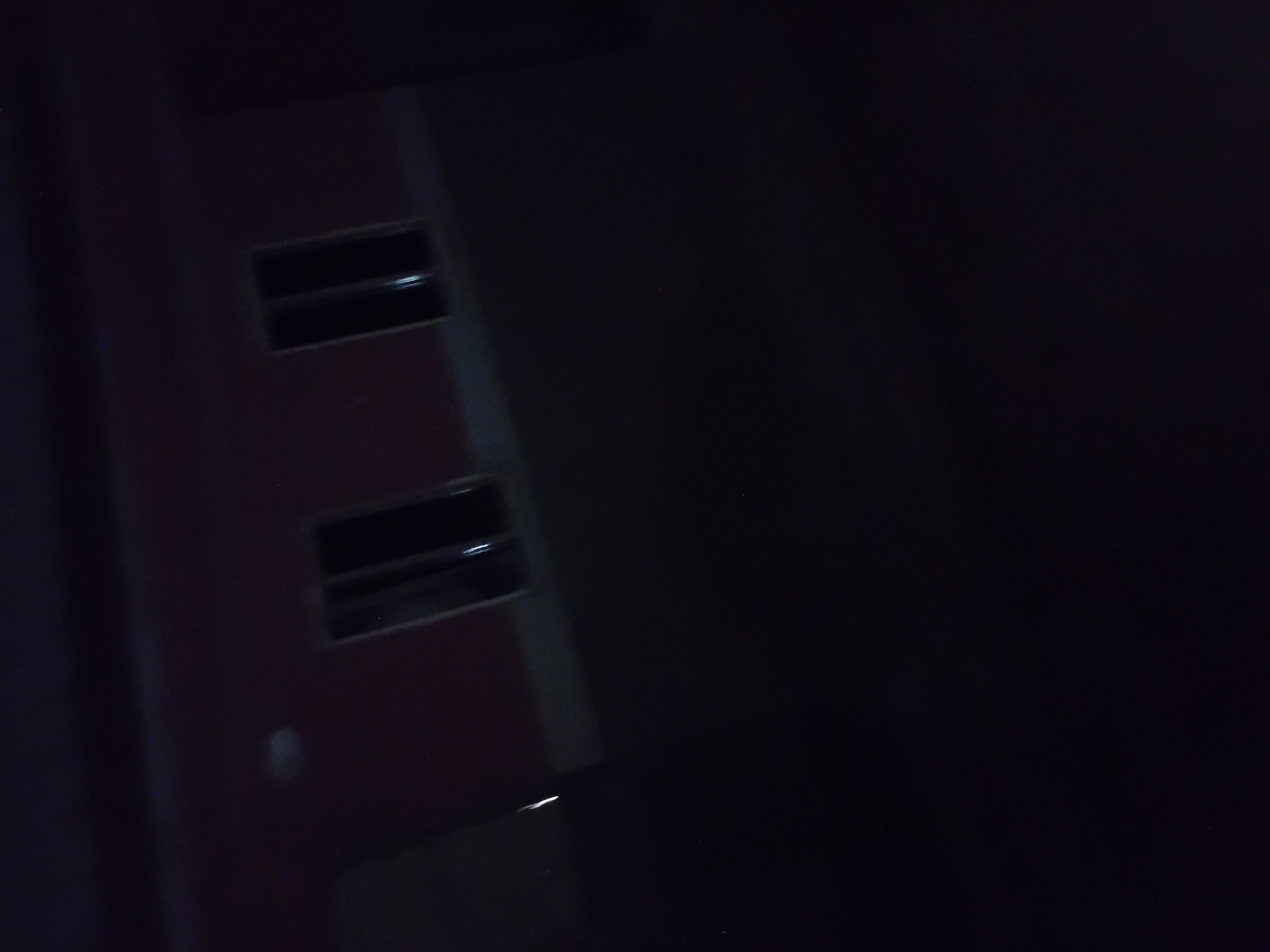 A blurry, dark image shows a red building with two dark windows. The building is likely a residential or commercial structure. The image is taken at night, as indicated by the darkness and the faint illumination from the windows. There are no people or specific actions visible in the image. The environment appears to be an urban setting, possibly a street or alleyway. The location in the city of Jauro Yinu, Nigeria, is unknown based on the visual information alone.