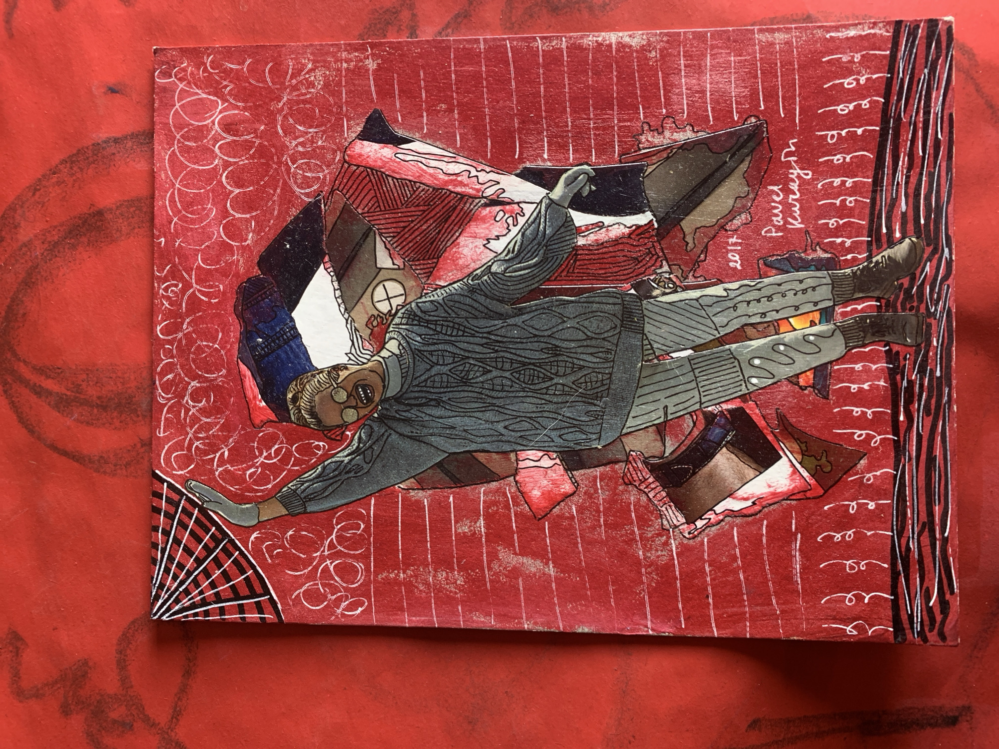 The image is a close-up, overhead shot of a piece of art on a textured red surface. The artwork depicts a stylized figure with blonde hair and round glasses, wearing a cable-knit sweater and striped pants. The figure is in a dynamic pose, with one arm raised and the other extended to the side. The background of the artwork is a collage of red, black, white, and blue paper fragments, with a recurring pattern of white, swirling lines. The bottom of the artwork features the signature "Pavel Kuraym" and the year "2017". The red surface underneath appears to have subtle darker red markings. The artwork is situated on a surface that resembles painted wood or canvas. There is no indication of the city of Sergeevo, Russia within the image itself.