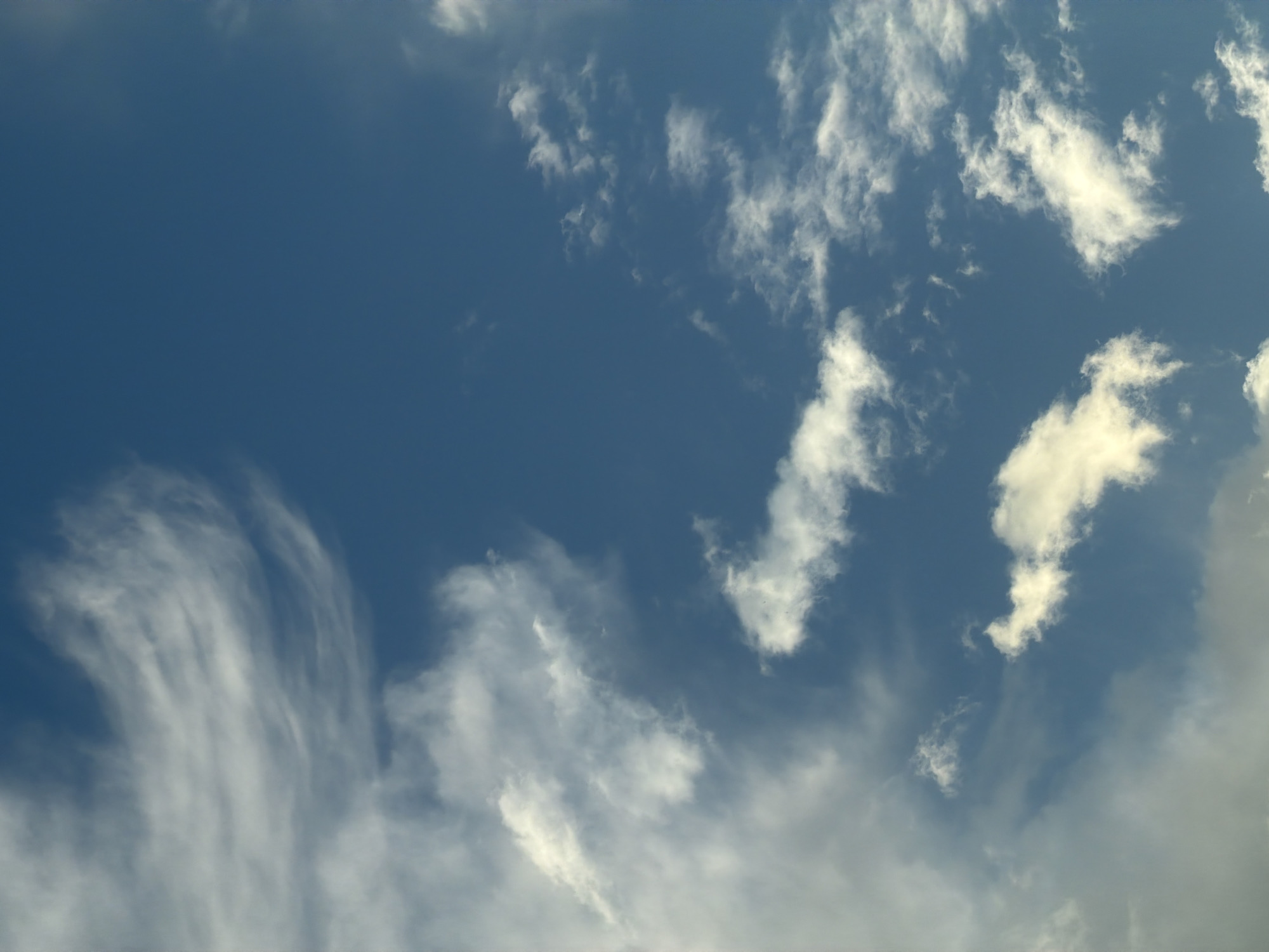 The image shows a daytime sky in Moscow, Russia. The sky is primarily a deep blue color. Wispy, white cirrus clouds are scattered throughout, with denser formations in the lower right and left portions of the image. There are no people, objects, or actions depicted other than the natural cloud formations within the environment of the sky.