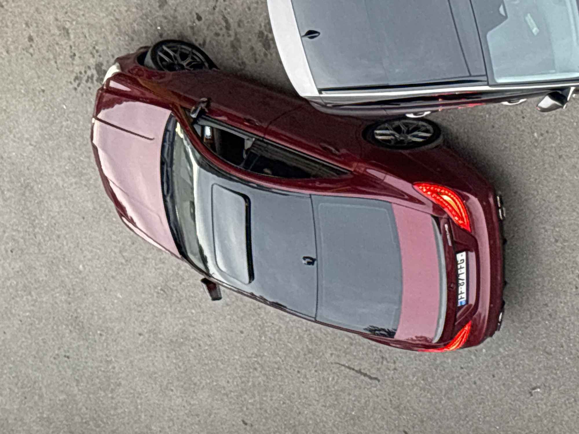 An overhead shot reveals a burgundy car parked close to a silver vehicle on an asphalt surface. The burgundy car has a sunroof, and its license plate reads "FF-871-FG". The exact location within Tbilisi, Georgia, is not identifiable from the image.