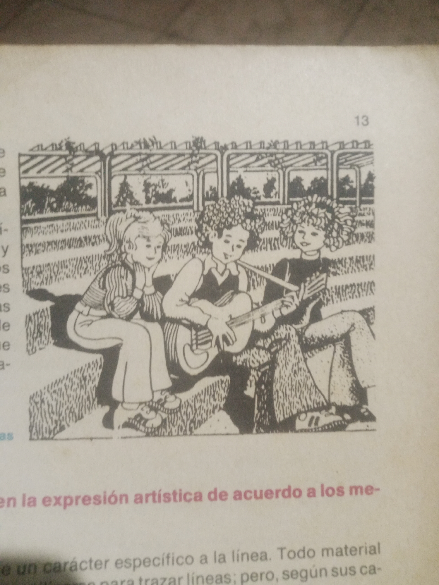 The image is a black and white drawing depicting three children sitting on a bench, possibly outdoors. Two of the children are playing music. The child on the left is holding a guitar, while the child in the middle appears to be playing a flute or recorder. The child on the right is looking towards the viewer. In the background, there is a structure that resembles a greenhouse or a covered walkway with plants inside. The image is accompanied by text, which is partially visible at the bottom of the frame and includes the number "13" at the top right. The scene does not contain any recognizable landmarks or details that would indicate its location in Santa Ana, Venezuela, or any other specific city.