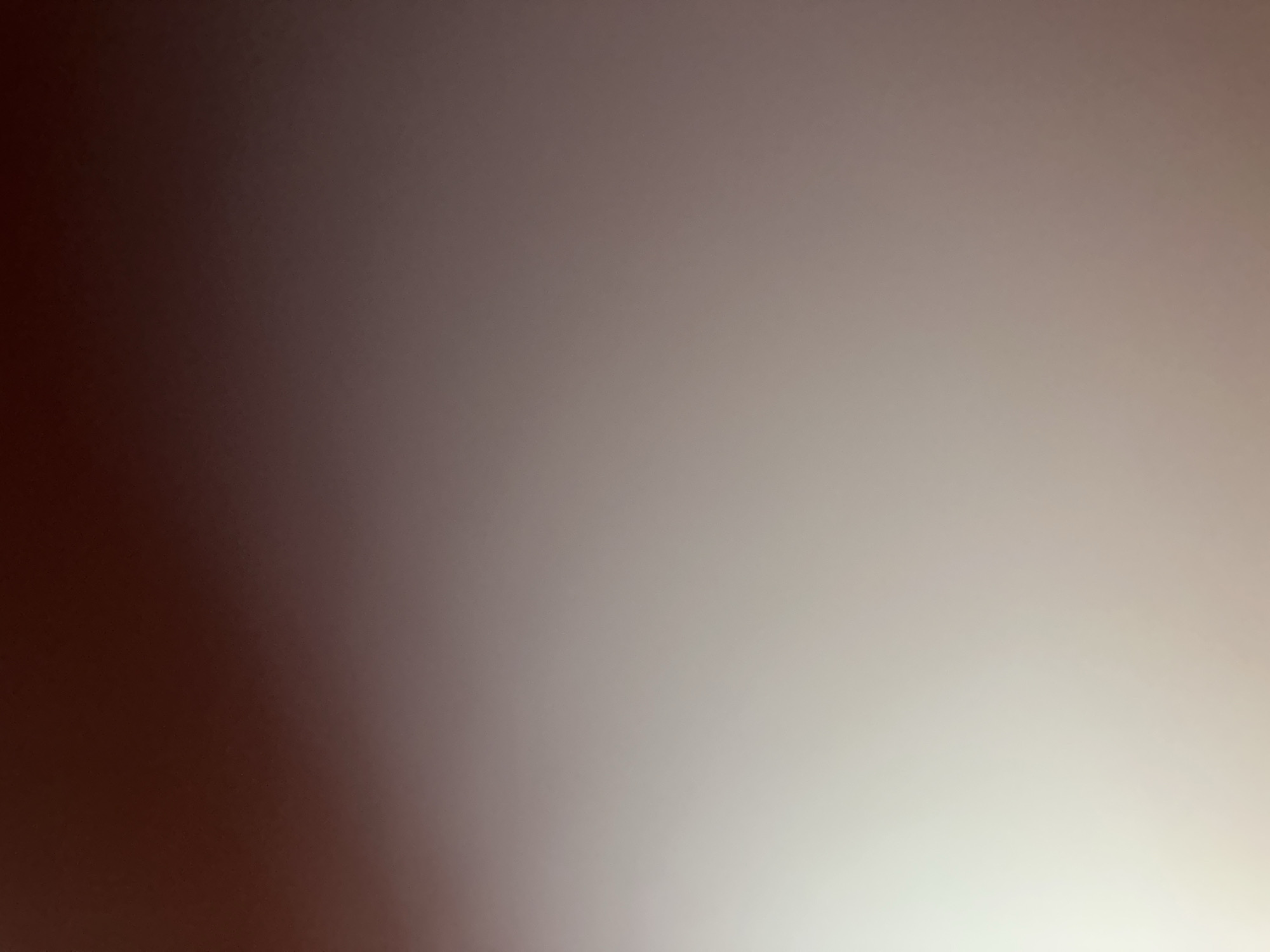 This is a close-up, abstract image with a smooth, gradient background. The image transitions from a dark, reddish-brown on the left side to a very light, almost white color on the right side, with shades of gray and beige in between. There are no discernible subjects, objects, or scenes. The lighting appears to be soft, creating a gentle fade across the frame. The texture of the background is uniformly smooth, suggesting it might be a digital creation or a photograph of a plain surface. There are no visible text, time of day indicators, weather cues, location cues, or emotions conveyed by the image. The abstract nature of the image makes it difficult to assign a specific activity or event.