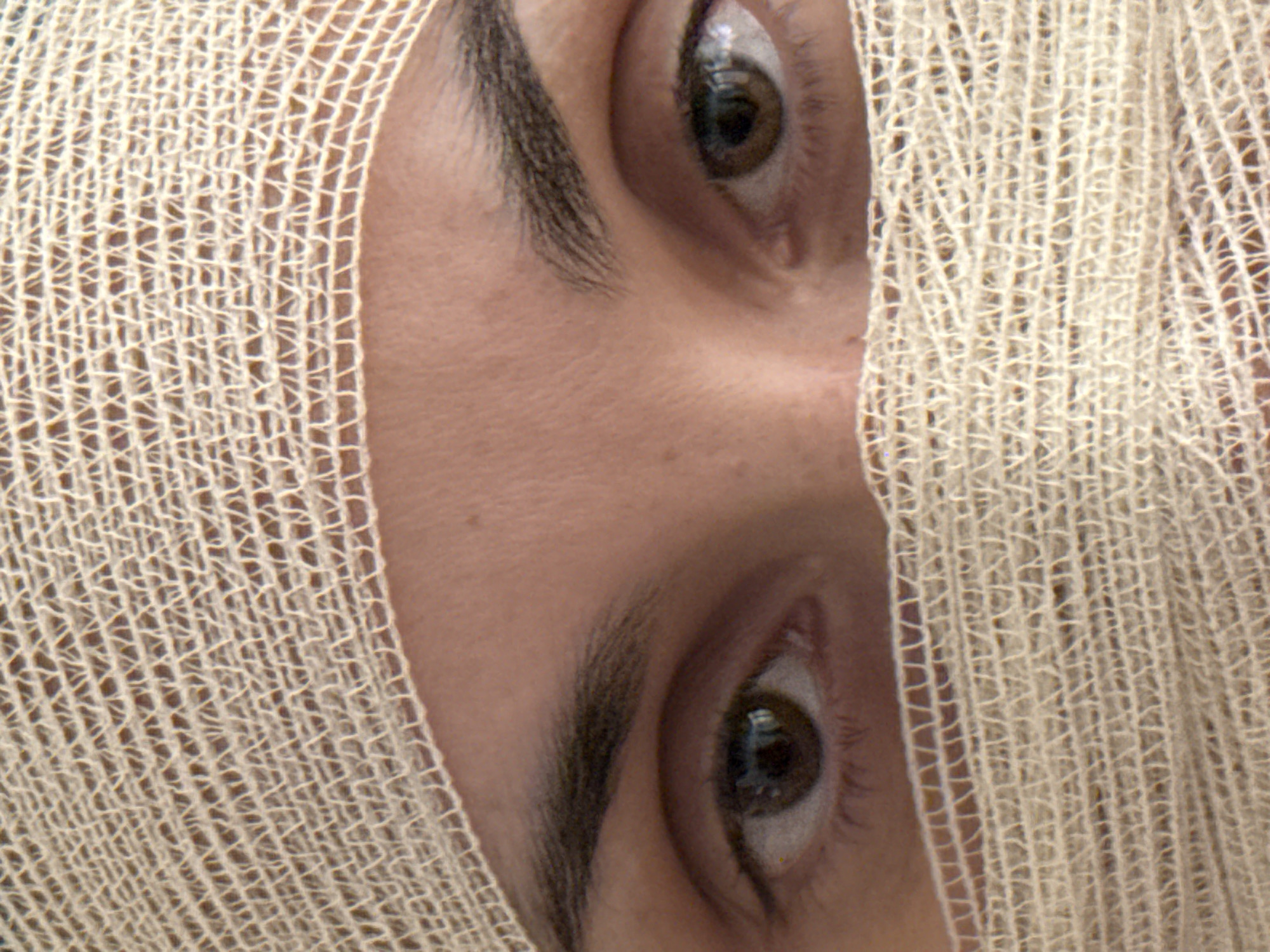 A close-up shot depicts a person's face, primarily focusing on the eyes, which are partially obscured by a light-colored, woven material resembling gauze or netting. The skin is light-toned, with visible eyebrows. There is no indication of a location in Pleven, Bulgaria.