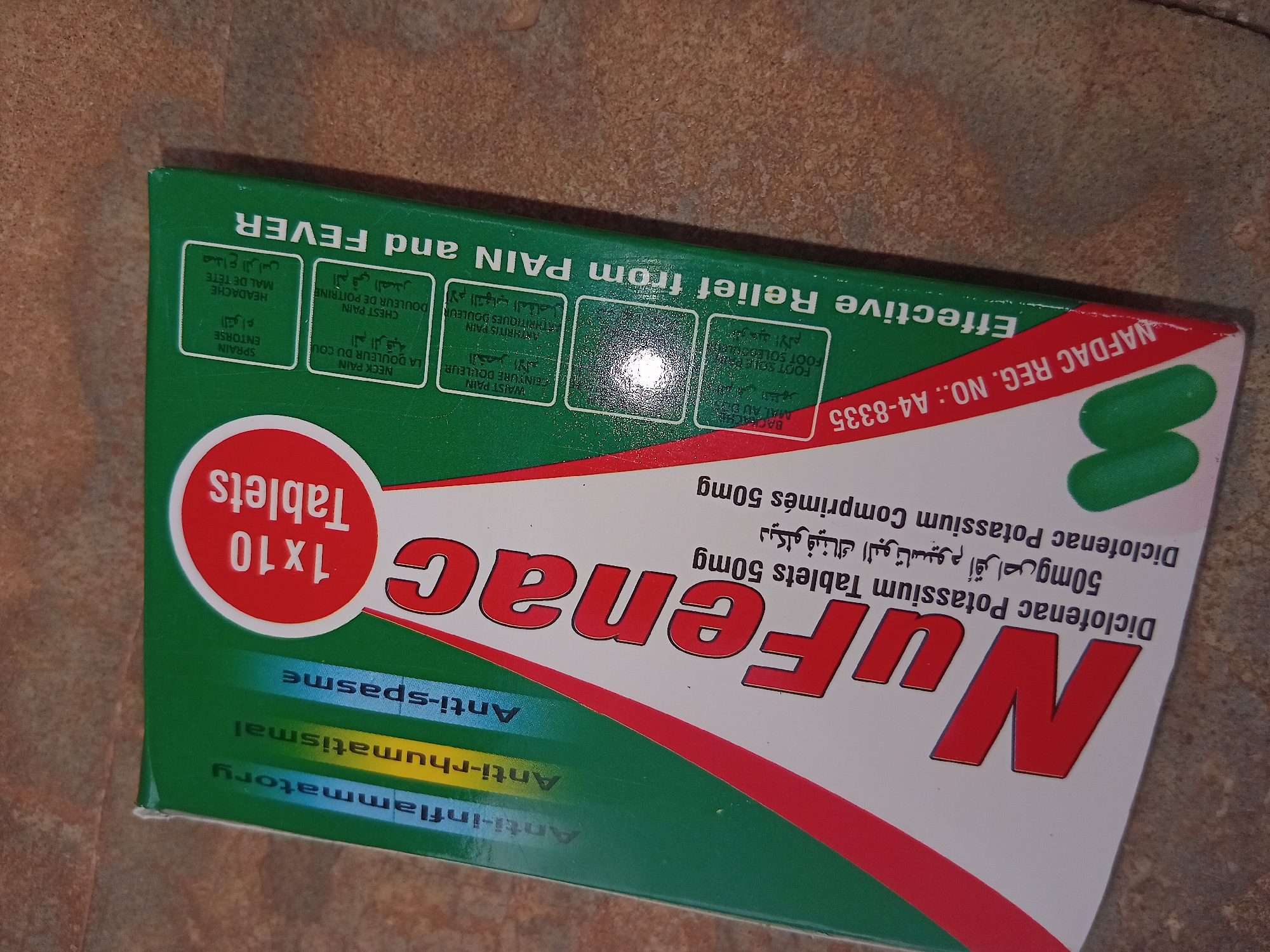 The image is a close-up shot of a box of "Nufenac" brand medicine. The box is mostly green with red and white accents. The brand name "Nufenac" is prominently displayed in red lettering. The box also contains information about the medication, including "Diclofenac Potassium Tablets 50mg" written in English and Arabic. Below the brand name, the box lists "Anti-inflammatory", "Anti-rhumatismal", and "Anti-spasme". The box has a "1x10 Tablets" logo. Along the top edge, "Effective Relief from PAIN and FEVER" is written in green, and there are also descriptions in English, French and Arabic of the type of pain from which the medicine provides relief: back ache, waist pain, foot sole pain, arthritis pain, chest pain, neck pain and headache. There is a "NAFDAC REG. NO.: A4-8335" which suggests the medicine is registered with the National Agency for Food and Drug Administration and Control in Nigeria.
The location of the image is not specified. Therefore I cannot provide the city of Shagamu, Nigeria.