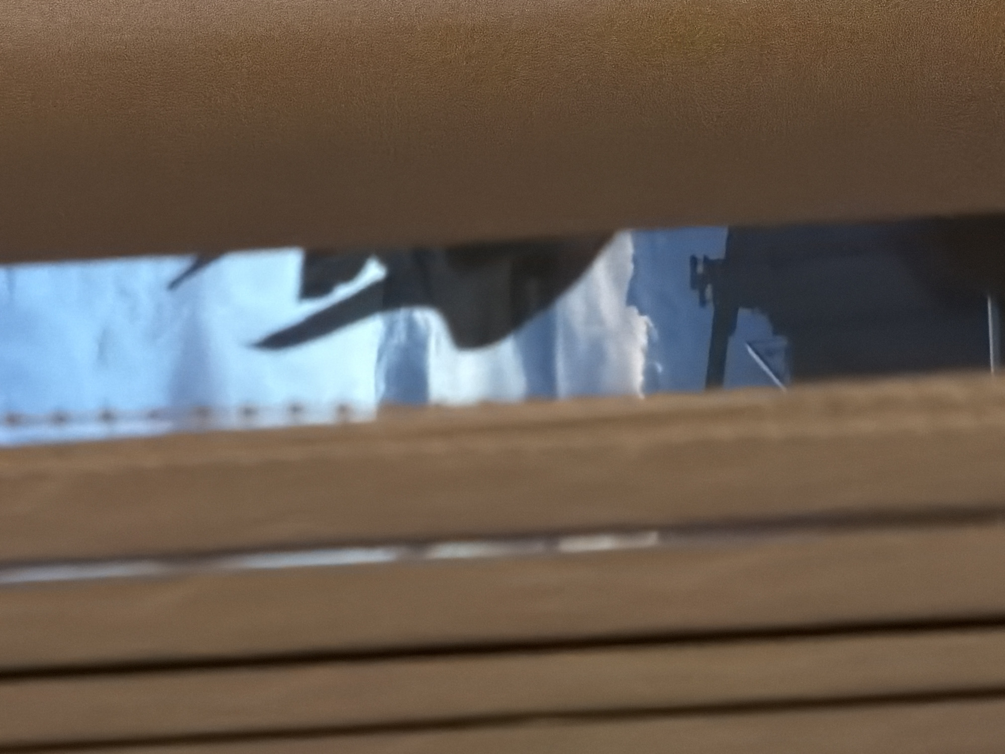 The image shows a view through partially closed blinds. Outside, the sky is visible with white clouds. Part of a crane is also visible. The location is indeterminable from the image, so I cannot confirm if it's in Plovdiv, Bulgaria.