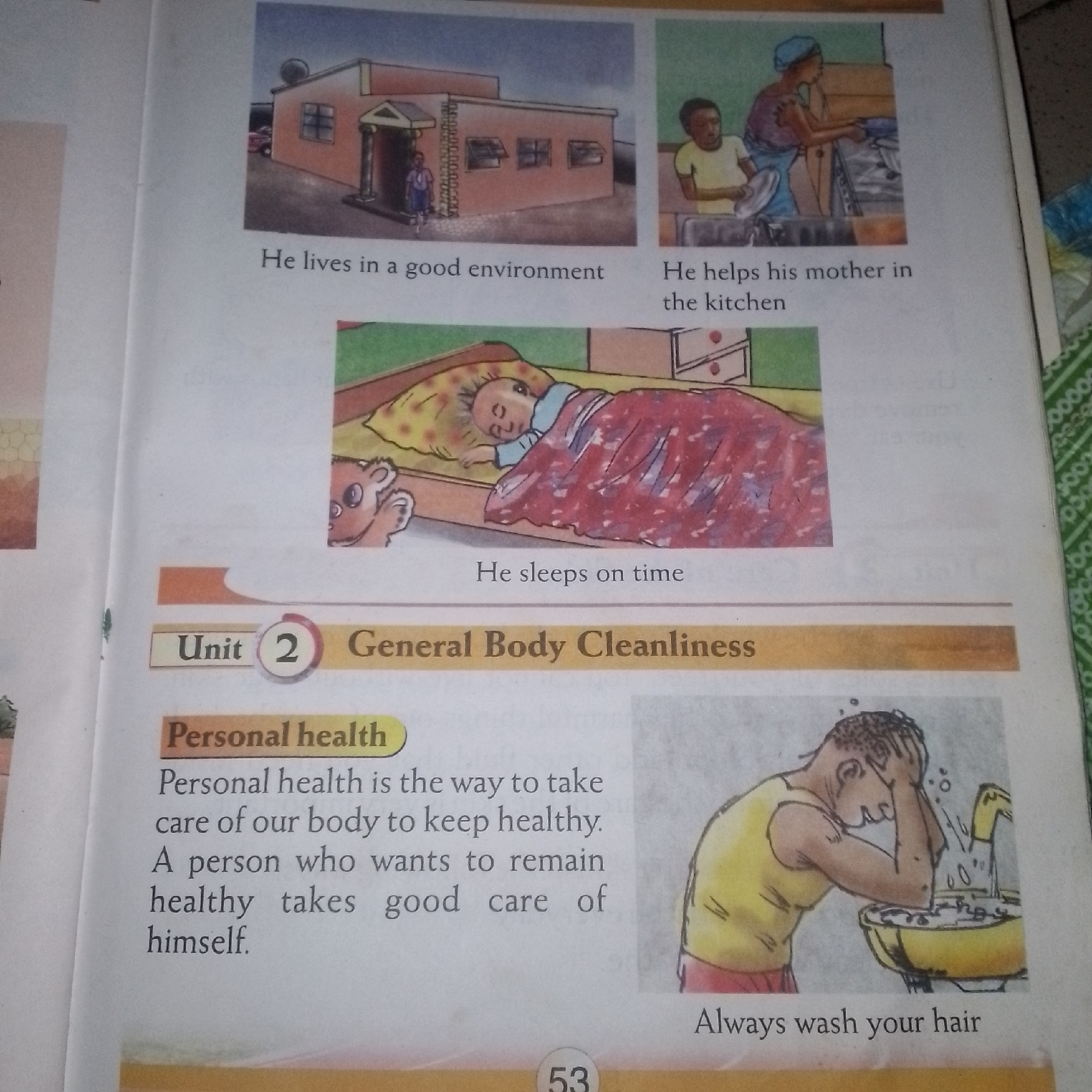 The image is a page from a children's book. At the top, there are two illustrations. The left illustration depicts a boy in a uniform standing outside a building that appears to be a school or a house. The text below reads "He lives in a good environment." The right illustration shows a woman and a boy in a kitchen, with the woman washing dishes and the boy helping. The text below this image states, "He helps his mother in the kitchen."
Below these illustrations is another picture of a baby sleeping soundly in a bed, with a teddy bear peeking out from the side. The caption reads, "He sleeps on time."
Further down the page, there is a section titled "Unit 2 General Body Cleanliness." Under this heading, there is a subsection labeled "Personal health." The text in this subsection defines personal health as "the way to take care of our body to keep healthy. A person who wants to remain healthy takes good care of himself."
To the right of the "Personal health" text, there is an illustration of a person washing their hair at a sink. The caption below this image says, "Always wash your hair." At the bottom center of the page, the number "53" is visible, indicating the page number. The background of the page is white, with some illustrations and text. There is also a green patterned border on the right side of the page.