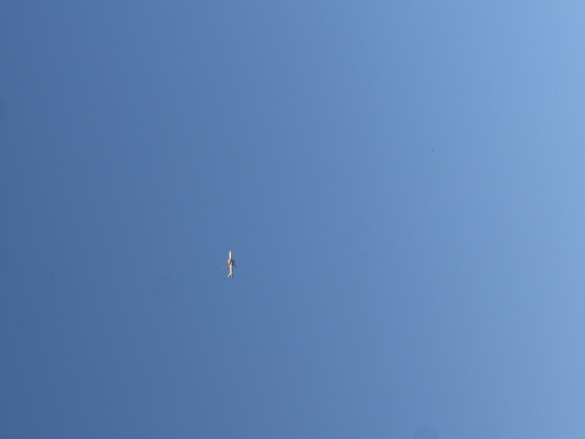 A white airplane is visible against a clear blue sky. The airplane is in the upper left quadrant of the image. There is no other discernable information in the image to indicate its location or time.