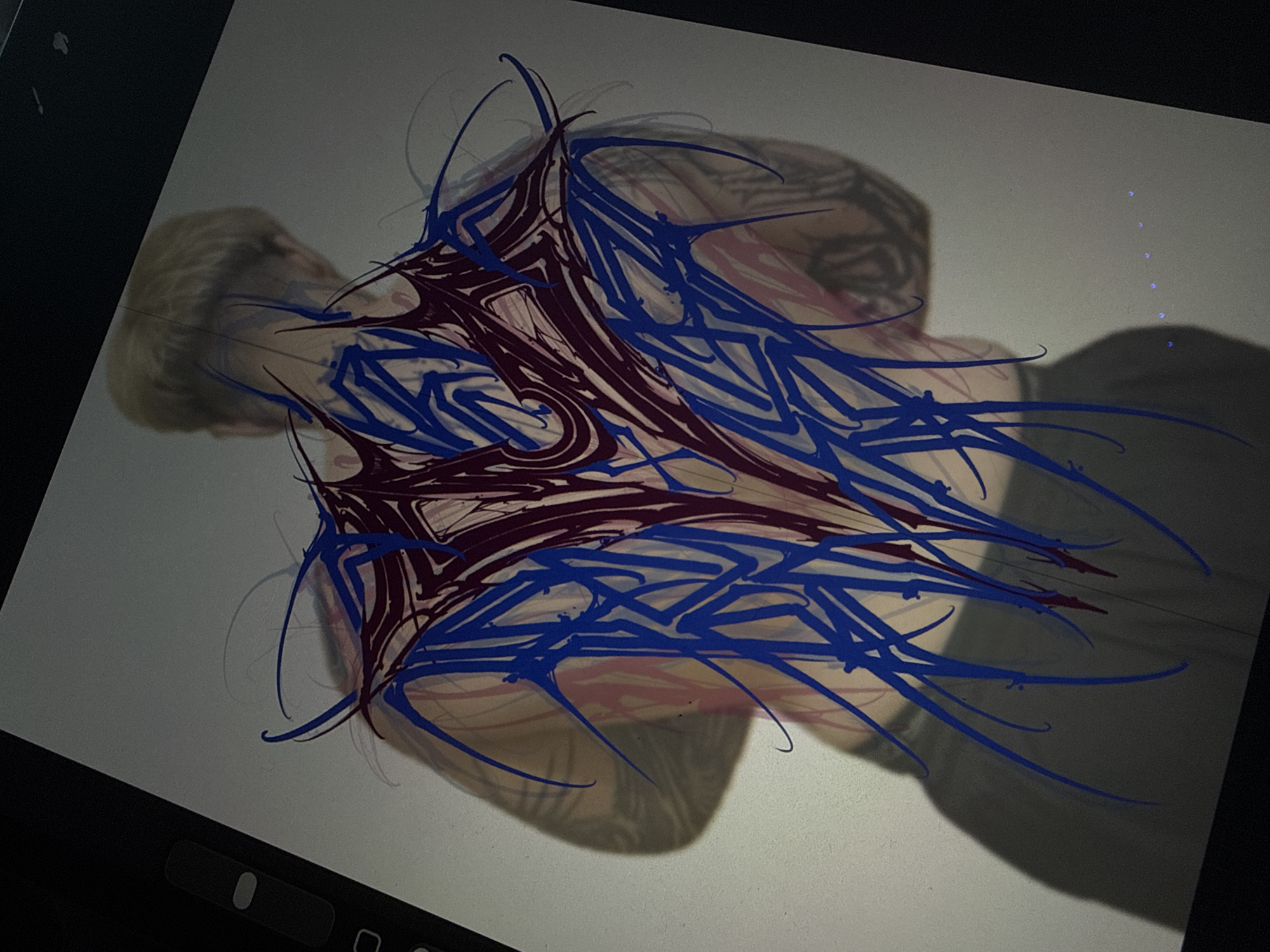 The image shows a tablet screen displaying a digital drawing. The drawing appears to be a stylized, abstract design in blue and dark red/purple, overlaid on a faint image of a person with tattoos lying down. The design is centered on the person's upper torso and back. The person's face is partially visible, appearing to have short blonde hair. The background of the tablet screen is light gray. A black border, assumed to be the edge of the tablet, is visible on the left and lower sides. There is no information in the image to locate it in Khimki, Russia.