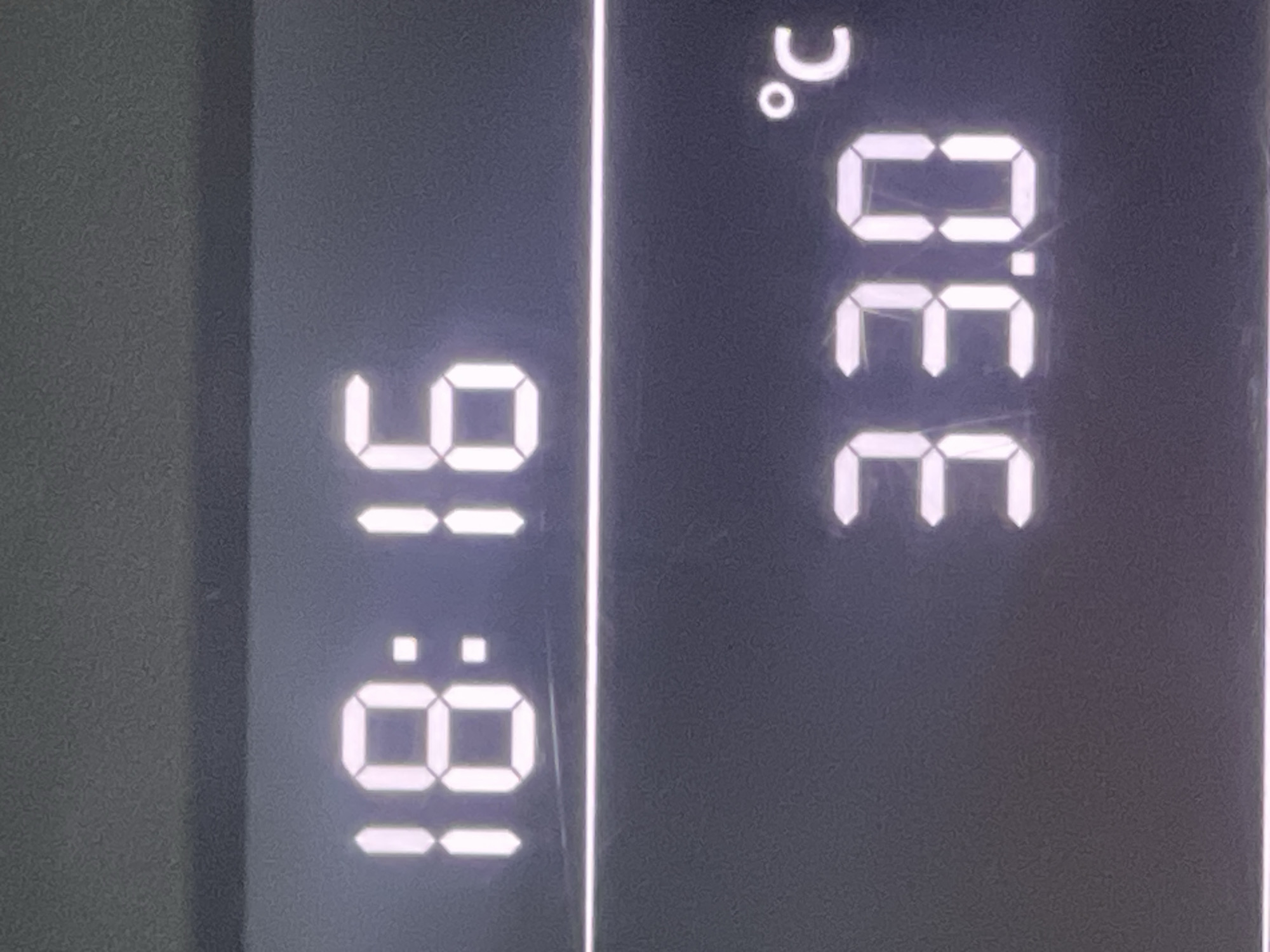 The image displays a digital screen showing the time and temperature. The time is 18:16 and the temperature is 33.0°C. The screen is likely from a car's dashboard or a similar digital display. The background is dark and slightly grainy. There are no people or other identifiable objects in the image. There is no information in the image that would indicate its location in the city of Ruse, Bulgaria.