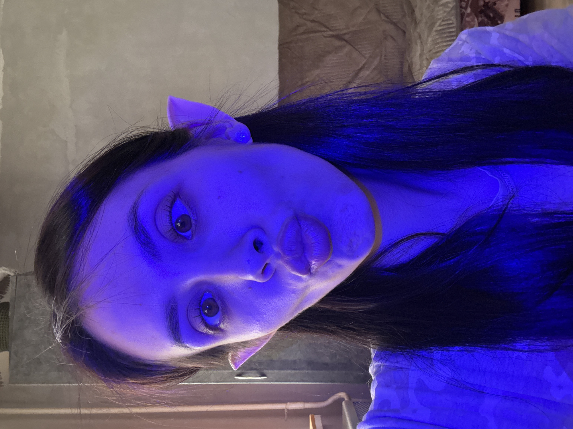 A woman with dark hair and pointed ears is visible in the image. The scene is lit with a strong blue light, obscuring details of her face and surroundings. Due to the lighting and angle, further details about the environment, location, objects, actions, and interactions are not ascertainable. There is no evidence in the image to place this in Votkinsk, Russia.
