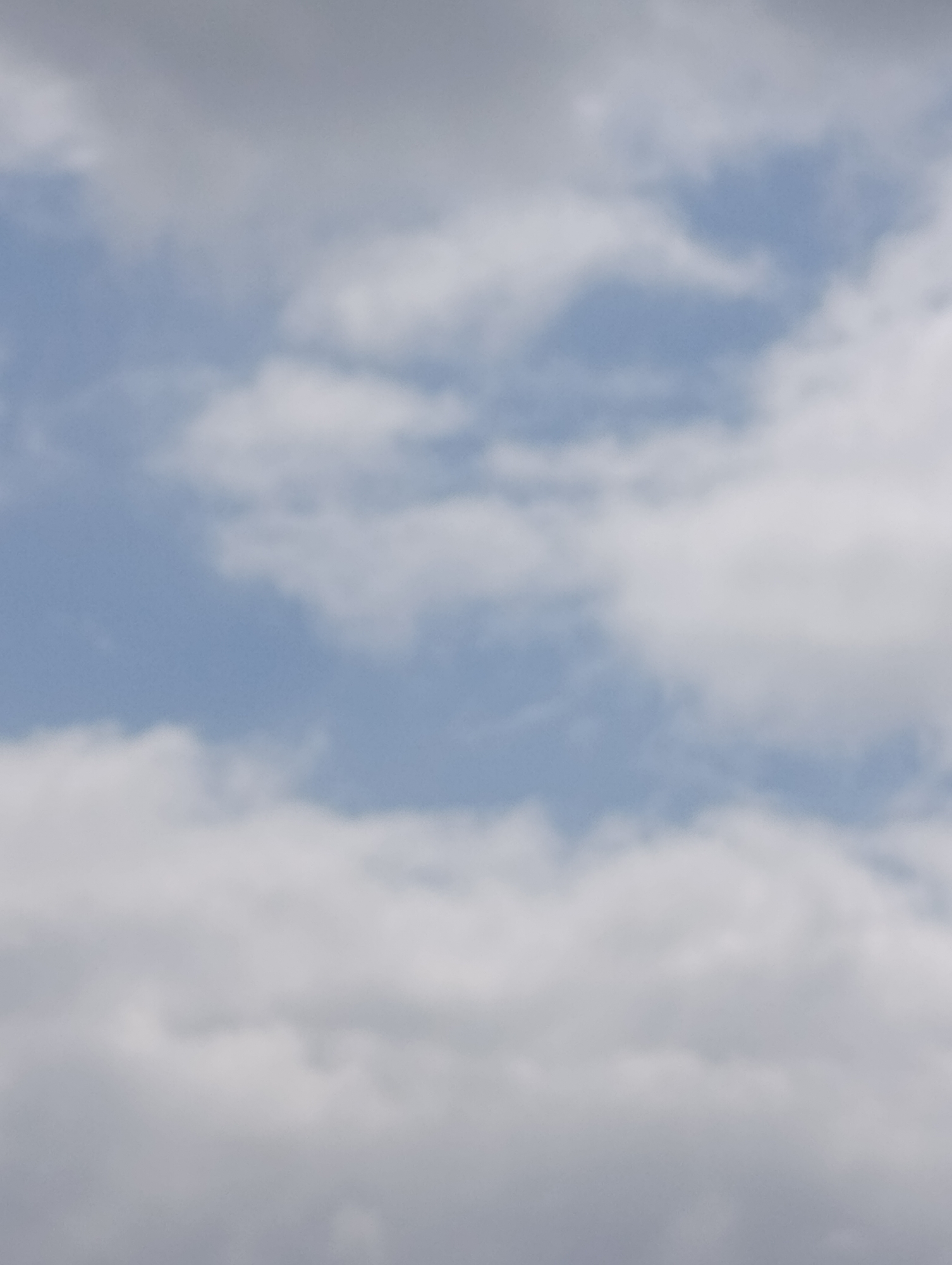 The image is a close-up, out-of-focus shot of a cloudy sky. The clouds are white and fluffy, with patches of blue sky visible in between. The lighting suggests it is daytime. The image does not contain any identifiable landmarks or features that would indicate a specific location within Setúbal, Portugal.