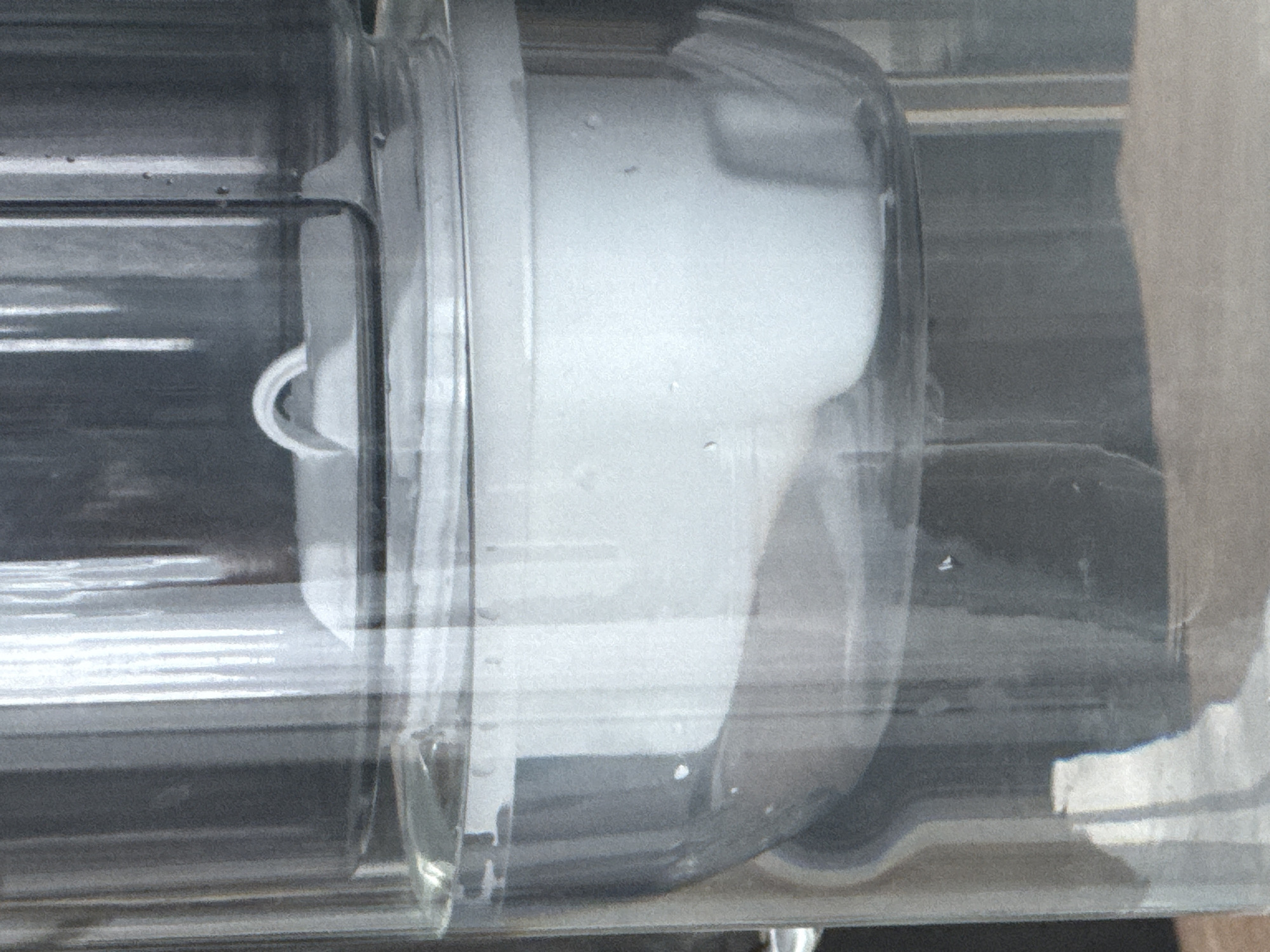 A close-up shows the interior of a clear, possibly plastic, container. Inside is a white, cylindrical object with a rounded end. Water droplets cling to the inside surface of the container. Horizontal lines are visible in the background, possibly part of the container's structure.