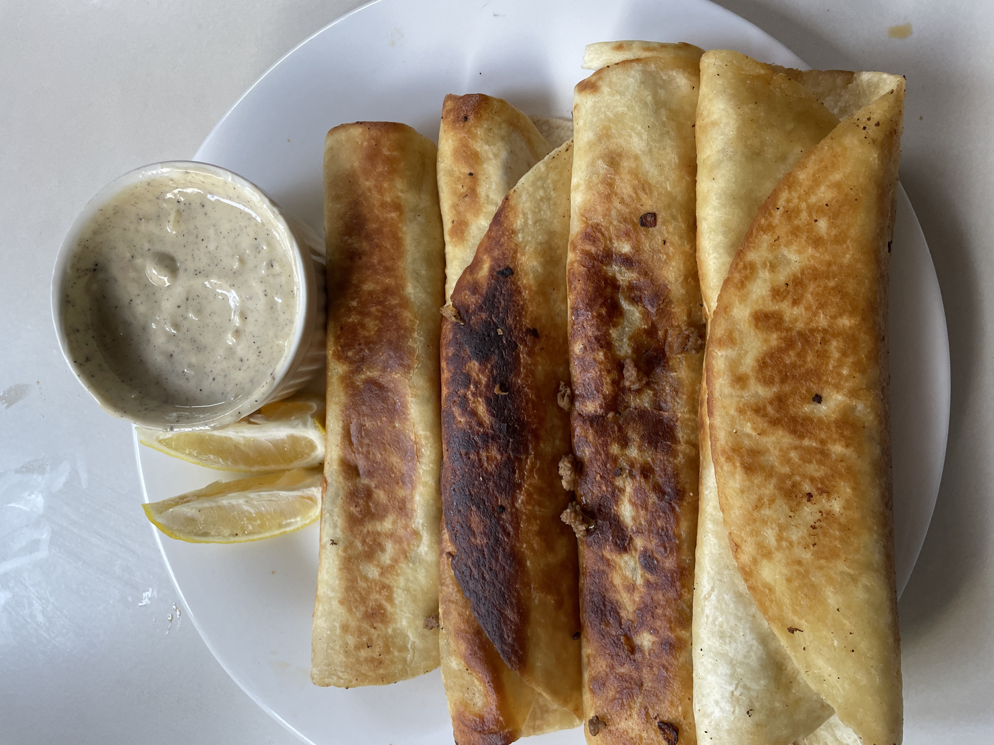 On a white plate are arranged four fried wraps, a small bowl of dip, and three lemon wedges. The wraps are golden brown, some darker than others, suggesting different levels of cooking. The dip is a light color with dark specks. The location is Davao City, Philippines.