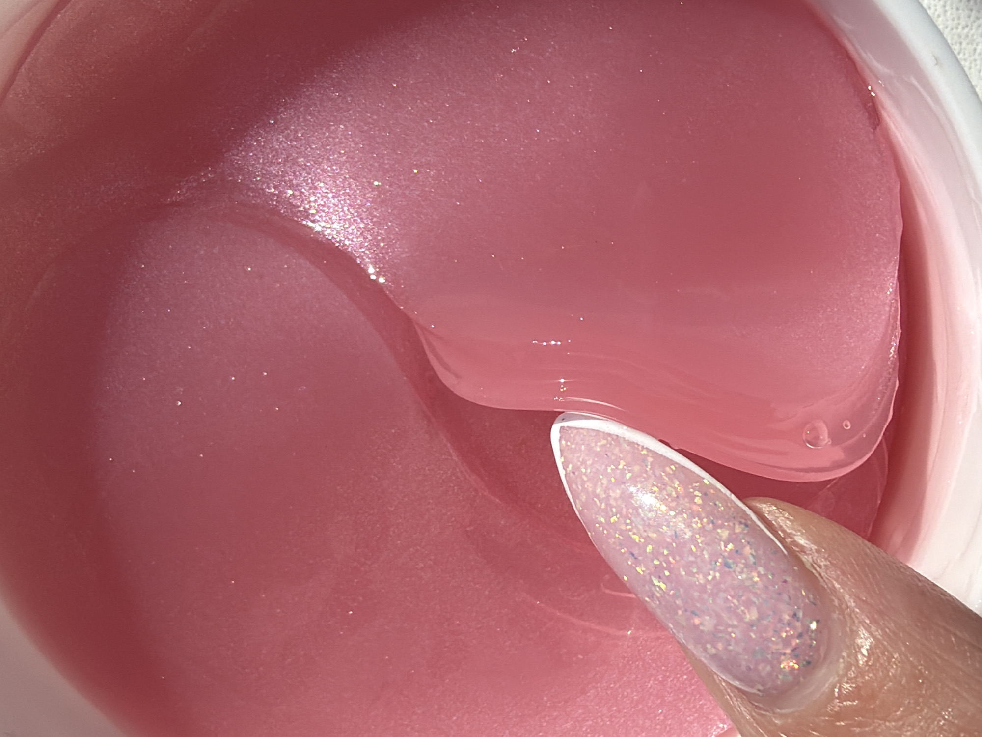A close-up shot shows a finger with a glittery nail dipping into a container of pink, gel-like substance, most likely cosmetic eye patches. The scene lacks any indication of location or specific details related to the city of Saint Petersburg, Russia.