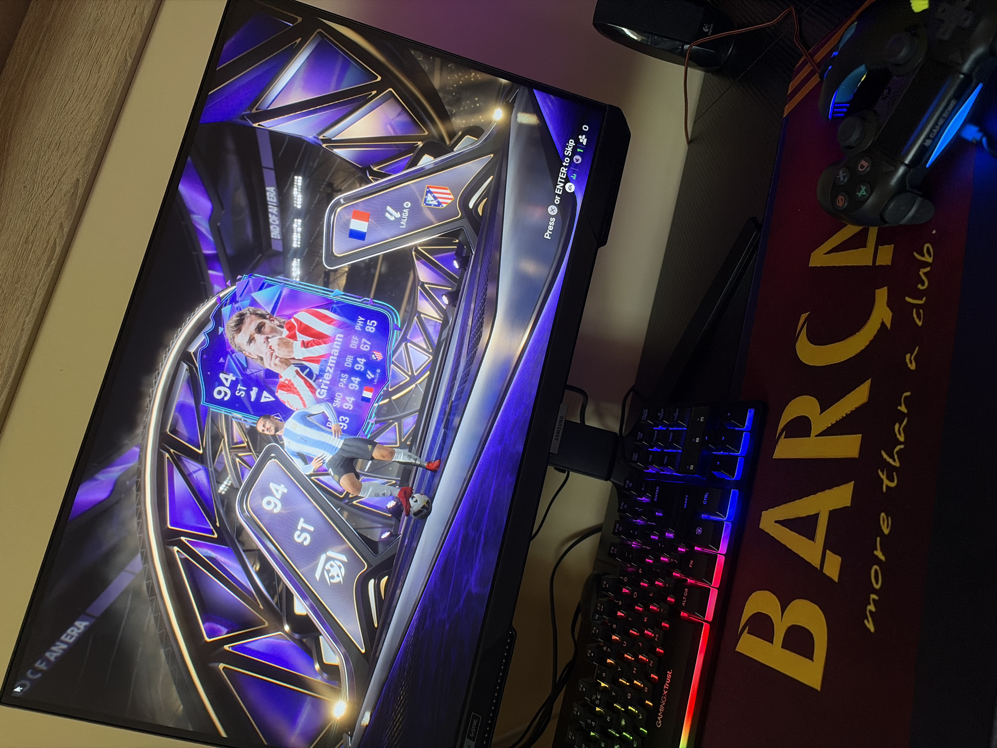 The image shows a gaming setup. A computer monitor displays a FIFA Ultimate Team card opening, featuring Antoine Griezmann. A keyboard with multi-colored backlighting sits on a mousepad branded with "BARCA more than a club." A gaming controller also lies on the mousepad. The location in Kozlovets, Bulgaria is not discernible from the image.