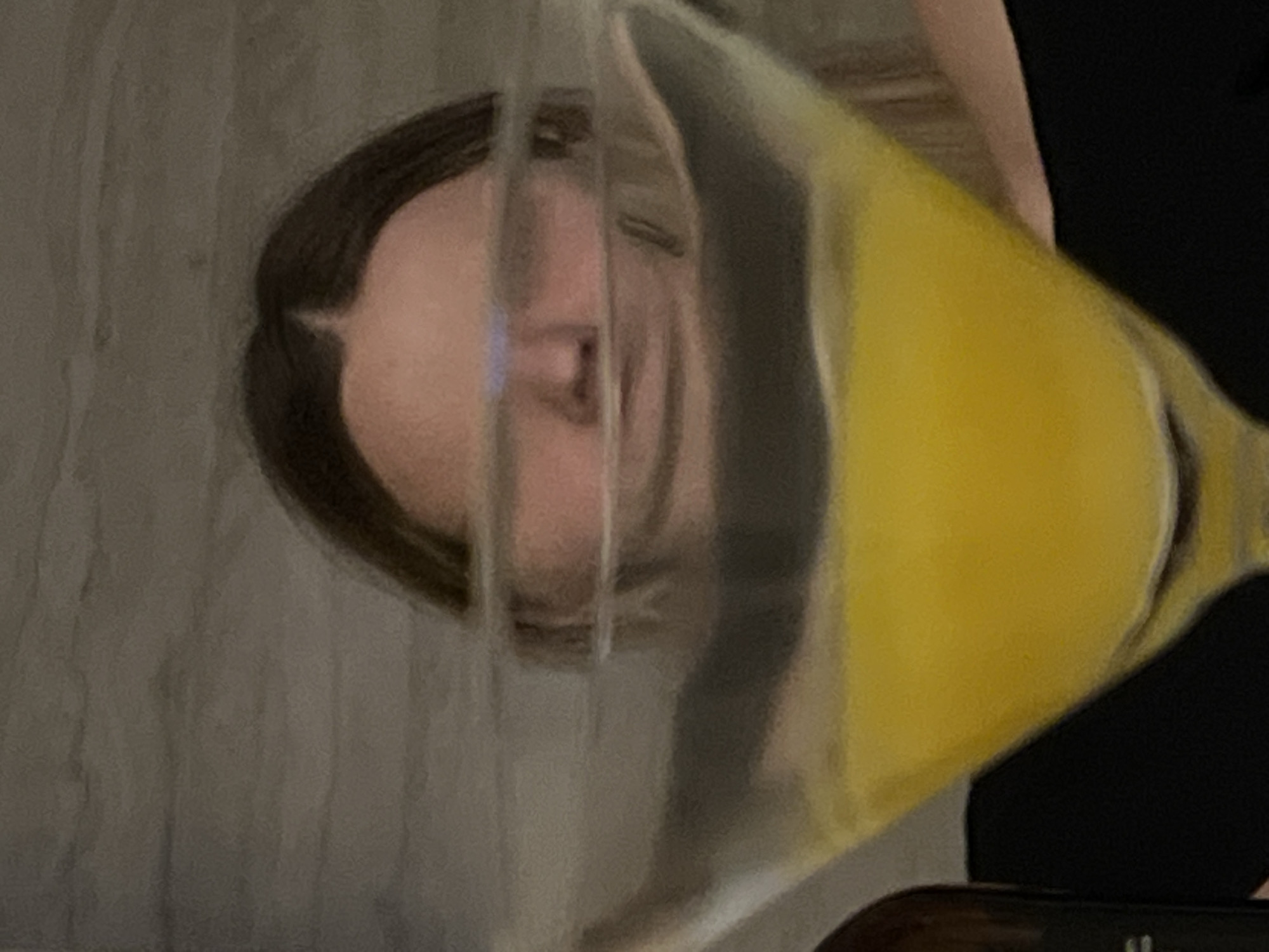The image depicts a person looking through a clear, filled container with a yellow liquid inside. The person has brown hair and appears to be indoors, with a textured gray surface behind them. The setting's location in Рубцово, Russia cannot be determined from the image.
