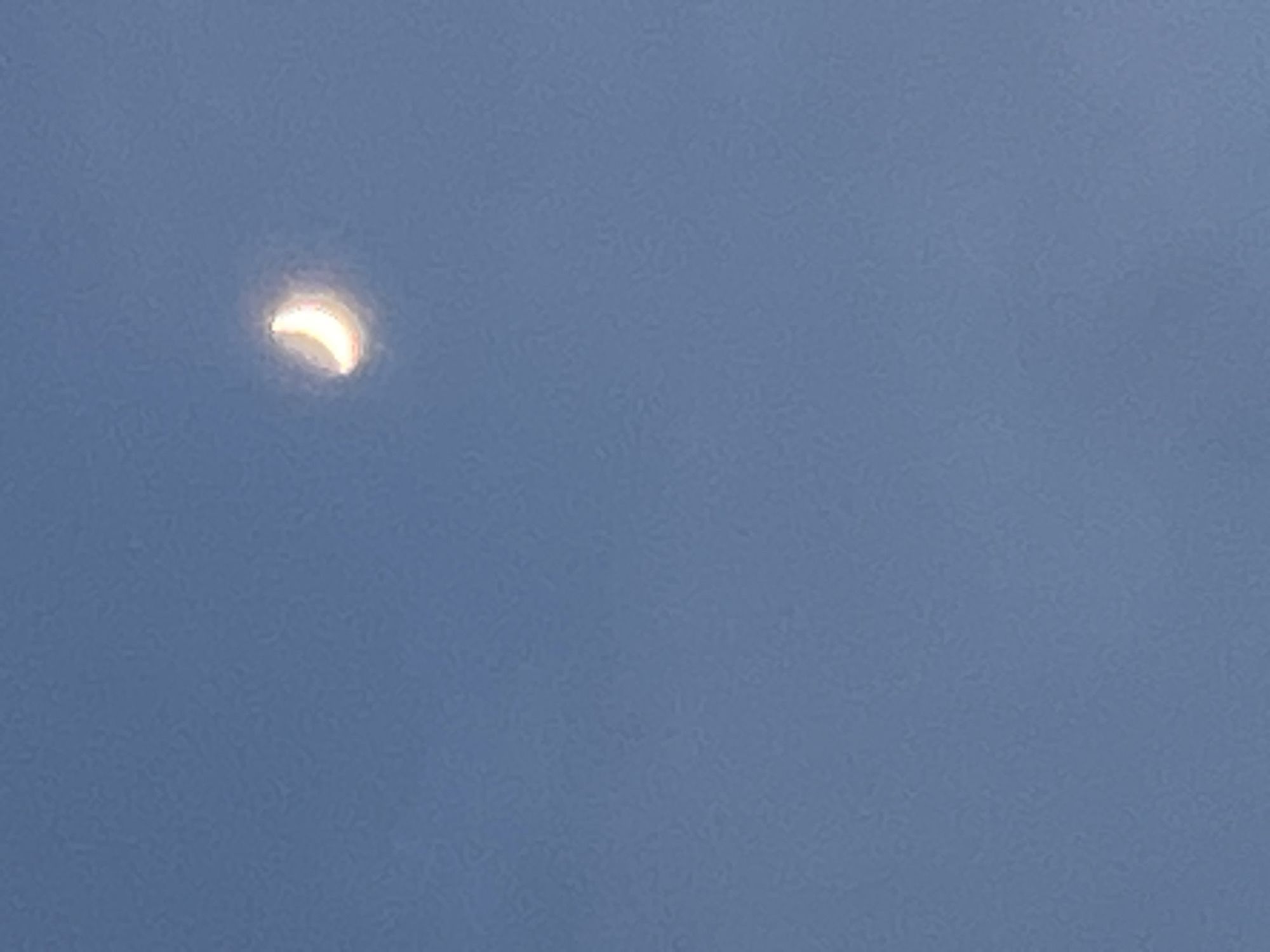 The image shows a crescent moon in a clear blue sky. The moon is located in the upper right portion of the frame and is illuminated from the right. The sky is a uniform blue color, with no other visible celestial bodies or atmospheric phenomena. The image appears to have been taken during daylight hours, as indicated by the blue sky. The specific location in Kara-Dıykan, Kyrgyzstan is not discernible from the image itself, as there are no identifying landmarks or contextual elements.