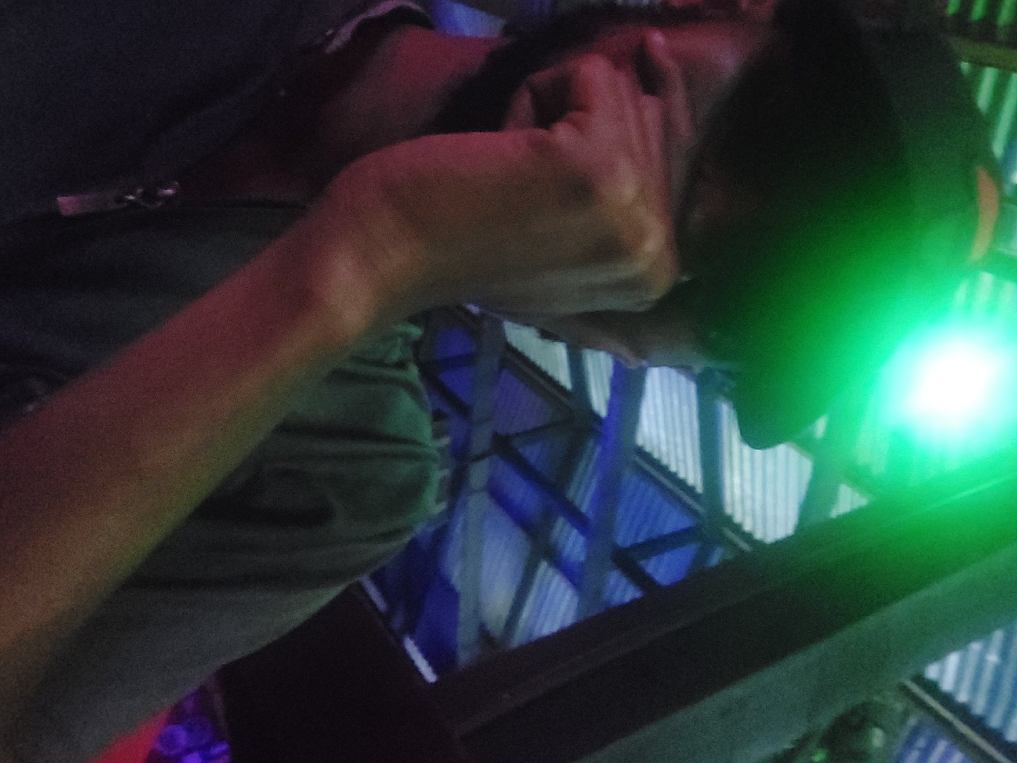 A person wearing a dark colored shirt or jacket is touching the side of their face or head with their right hand. The person is wearing a black cap or a hood over their head. The background appears to be the interior structure of a building, possibly a roof or ceiling, made of light blue and gray materials. An area of bright green light is also visible. I am unable to verify the location of Dar es-Salaam, Tanzania from this image.