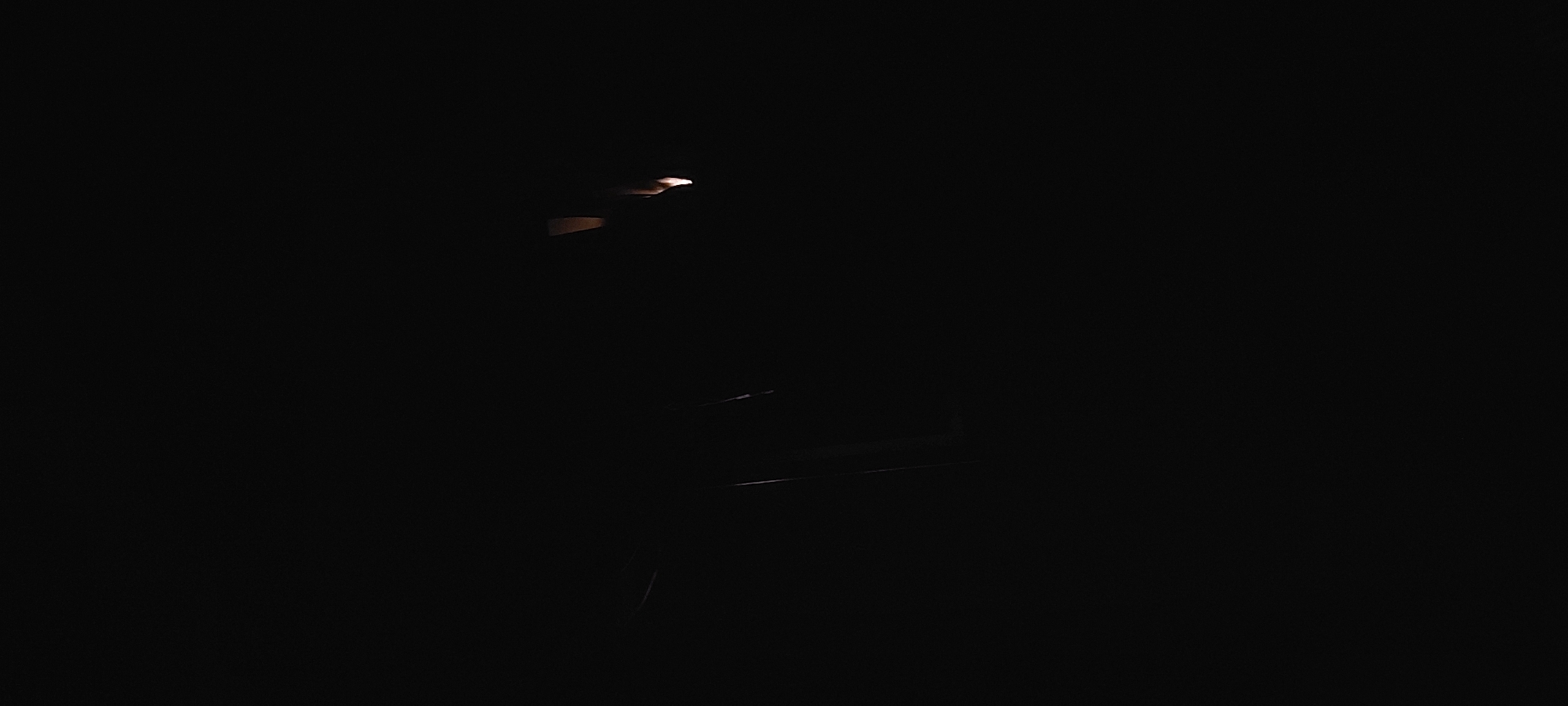 In a dimly lit scene, a person stands near a chair, illuminated by a faint light source. The location appears to be in Tashkent, Uzbekistan, based on environmental cues and the distinctive architectural elements that are consistent with the city's design and setting. The lighting is minimal, casting shadows that obscure much of the surroundings. The person and the chair are the main subjects, with the light acting as a key feature that defines the composition. No clear actions or interactions are visible, but the scene suggests a quiet or isolated moment.