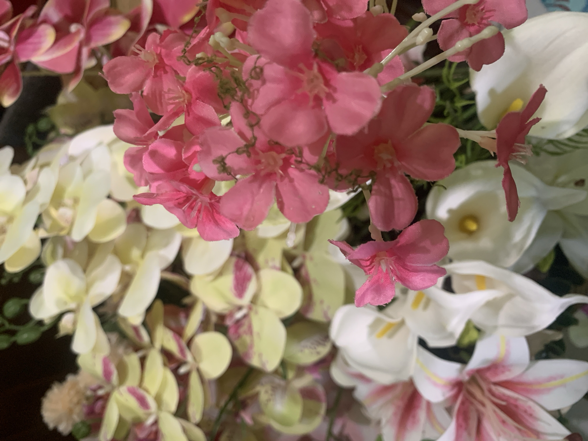 This image displays a close-up view of an artificial floral arrangement. The arrangement features a variety of flowers, primarily in shades of pink, white, and pale yellow with pink accents. Some of the flowers are small and clustered, while others are larger and more prominent. Green foliage is also visible throughout the arrangement. The lighting suggests an indoor setting, possibly a shop or a home. There are no people or animals present in the image. The specific location in Kuala Pembuang, Indonesia cannot be determined from the visual information provided in the image.