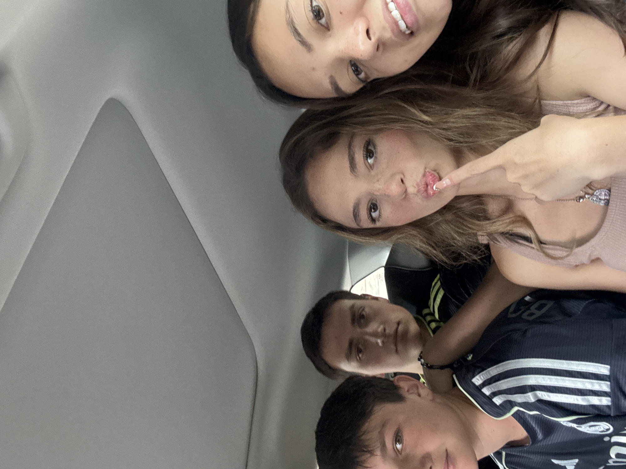 The photograph shows four individuals in what appears to be the interior of a car. At the top are two girls, one with dark hair and the other with light brown hair. The second girl points to her lips. Below them, two young men are visible, both wearing athletic shirts. The environment inside the car appears casual and informal, with a gray interior ceiling visible. There is no information in the image to indicate a specific location in San Bernardino Tlaxcalancingo, Mexico.