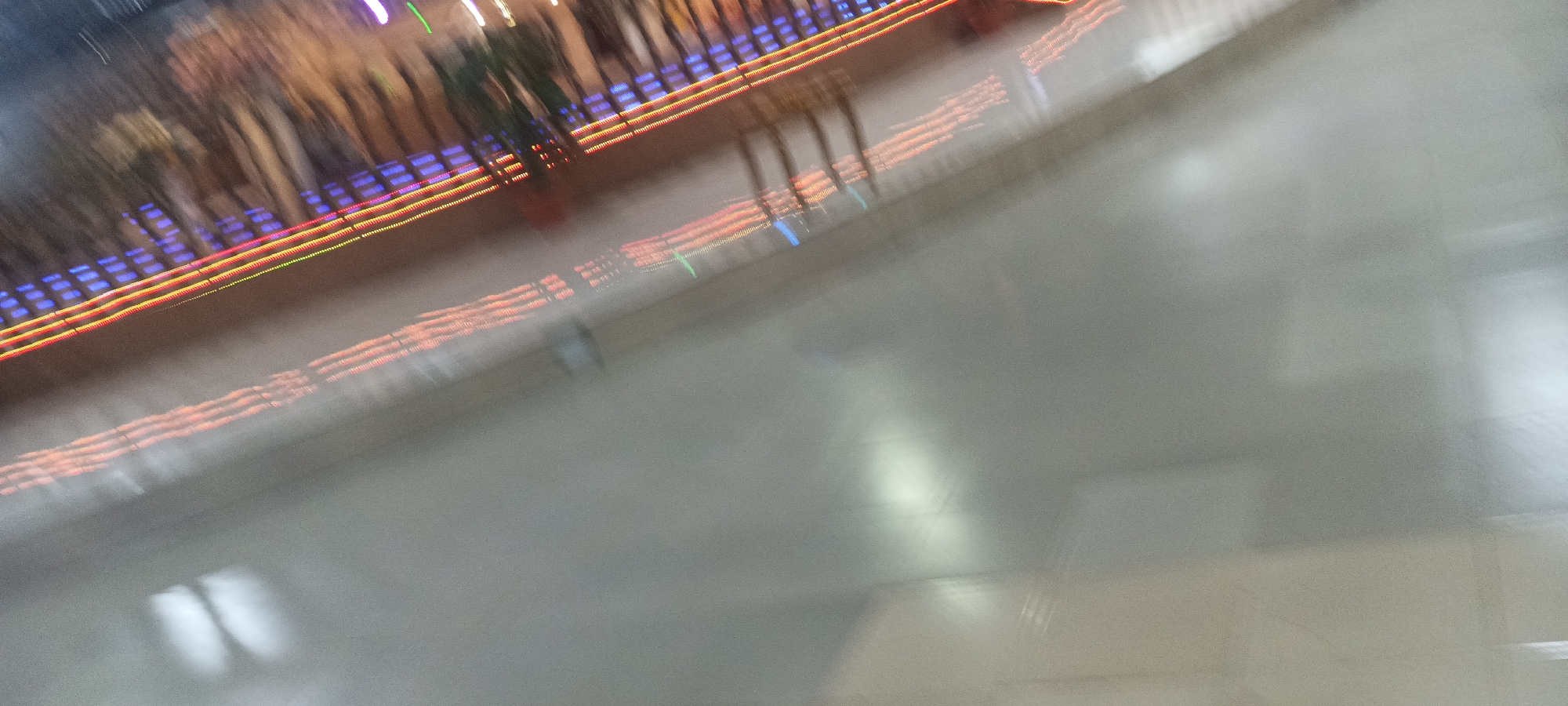 The image is heavily blurred, suggesting motion or poor focus. It appears to show an indoor scene with artificial lighting. There's a raised platform or structure with what seems to be a series of blue, red, and yellow lights. Vague, blurry figures suggest the presence of people. The location, Rukuba Road, Nigeria, is not discernible from this image alone. The majority of the image is filled with a grey, out-of-focus area, likely a floor or wall.