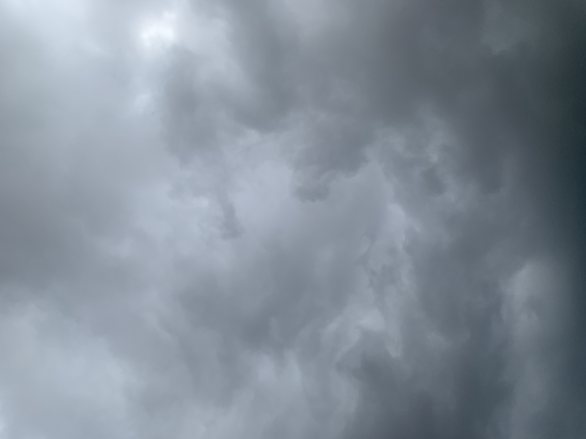 The image shows a dramatic sky filled with dark, turbulent storm clouds. The clouds are dense and heavy, with varying shades of gray, suggesting an impending storm or recent heavy rainfall. The lighting is diffused, creating a somber and somewhat ominous atmosphere. There are no discernible objects or people in the frame, focusing entirely on the natural phenomenon of the sky. The image appears to be a close-up view of the cloud formations, giving a sense of their immense scale and texture. There is no visible text in the image. The overall impression is one of raw, natural power and the dramatic beauty of a stormy sky.