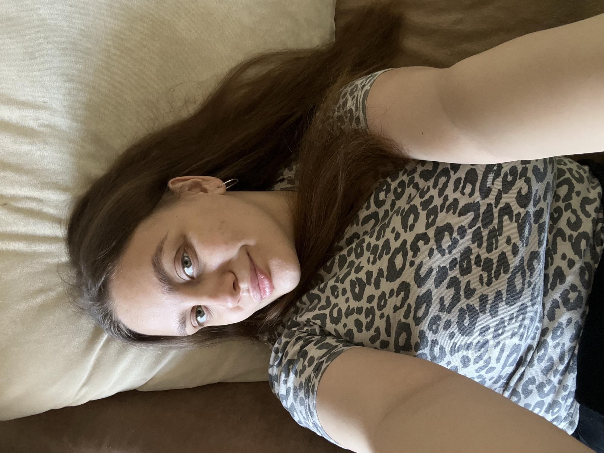 A woman with long brown hair and green eyes is lying on a light-colored pillow on a brown surface. She is wearing a gray and black leopard print shirt. The location cannot be determined as Chaikovsky, Russia.