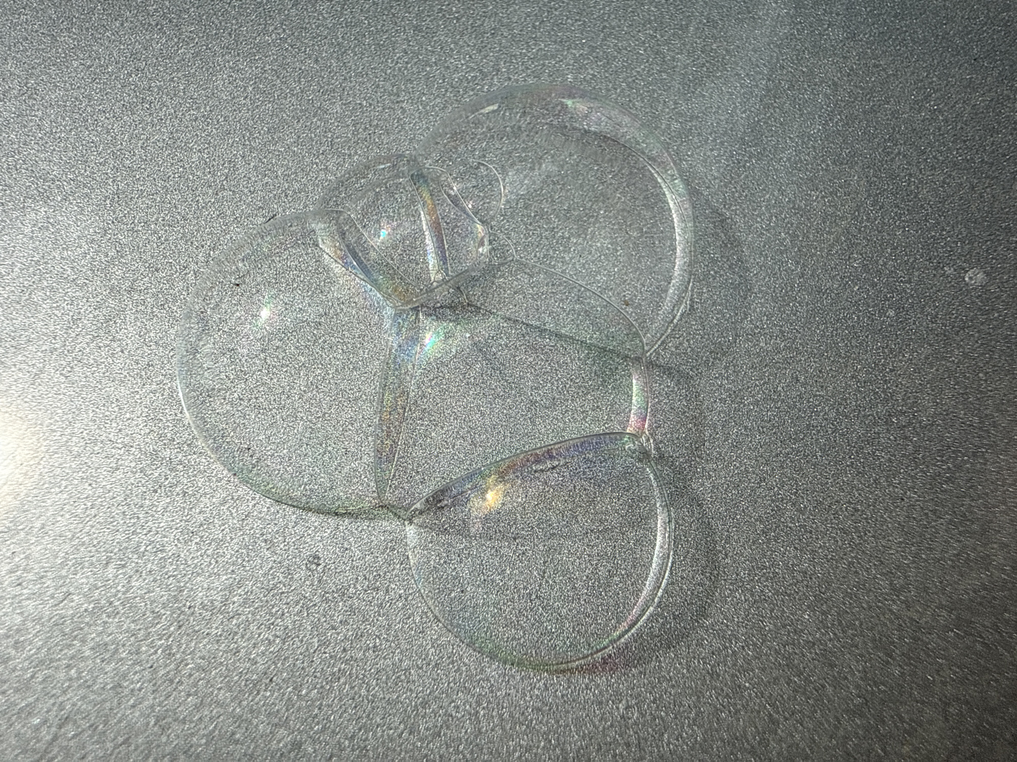 The image shows a cluster of soap bubbles on a textured gray surface. The bubbles overlap and intersect, creating iridescent reflections of light. The scene appears to be indoors, with artificial lighting. There are no people or other identifiable objects visible. The location is not identifiable as Noviy, Russia, or any specific place.