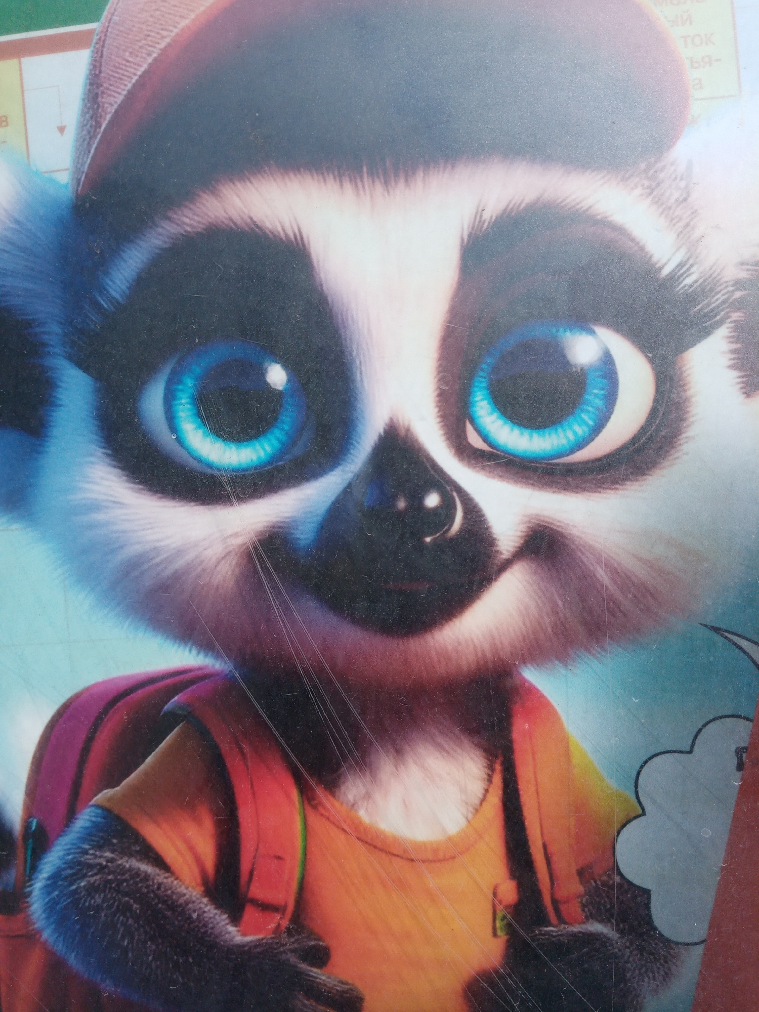 The image depicts a cartoon lemur wearing a backwards baseball cap and a backpack. The lemur has large, blue eyes, a black nose, and white fur. It is wearing an orange shirt. The background is blurred and appears to be a light blue color. There are scratches and other marks on the image, suggesting it may be a photograph of a printed image. The location, Elektrostal, Russia, is not visually discernible from the provided image.