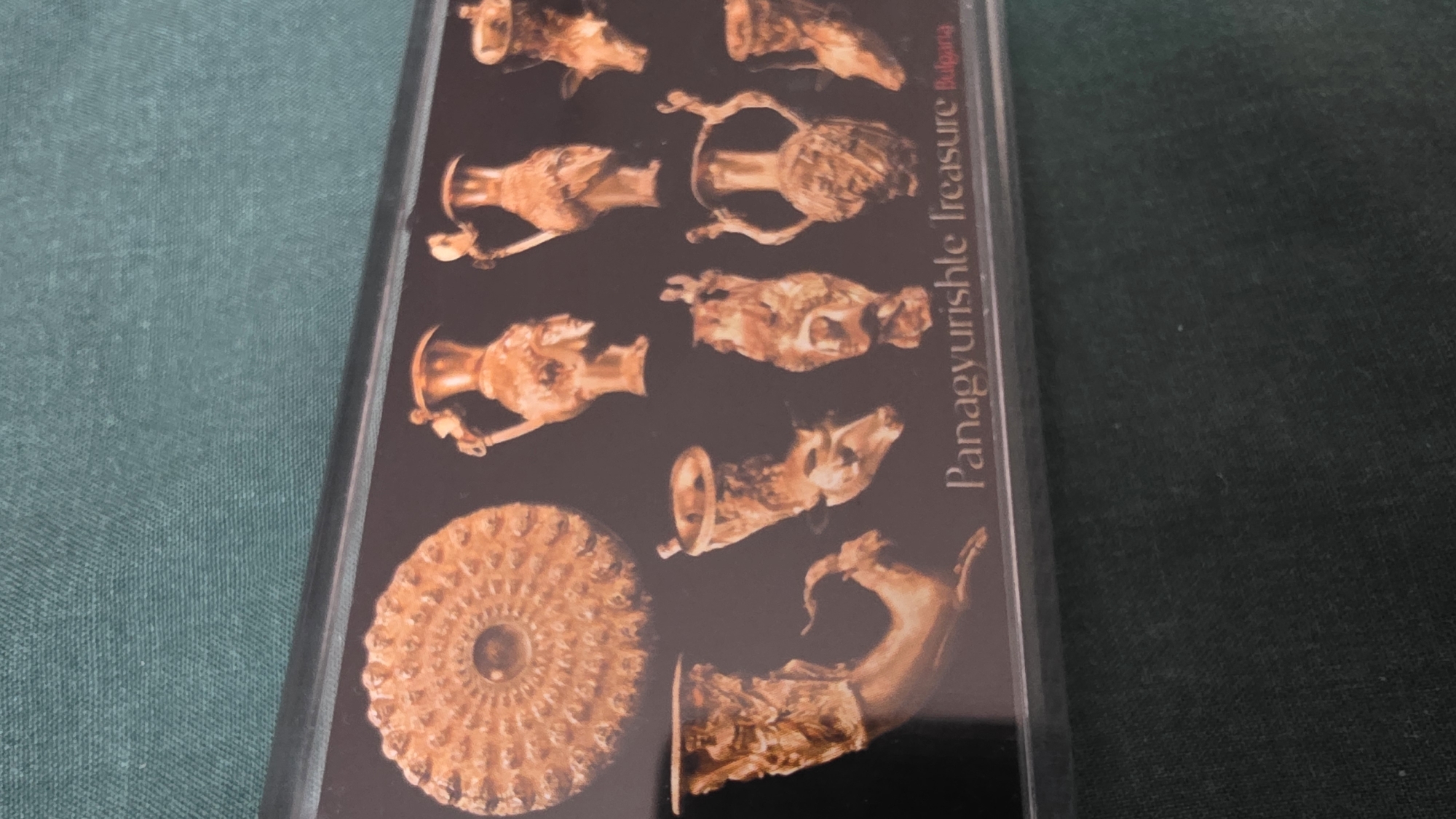 The image shows a postcard featuring the Panagyurishte Treasure, a Thracian gold treasure found in Bulgaria. The text "Panagyurishte Treasure Bulgaria" is printed on the card. The postcard displays a collection of golden artifacts. The location is not in Blagoevgrad, Bulgaria, but rather Panagyurishte.