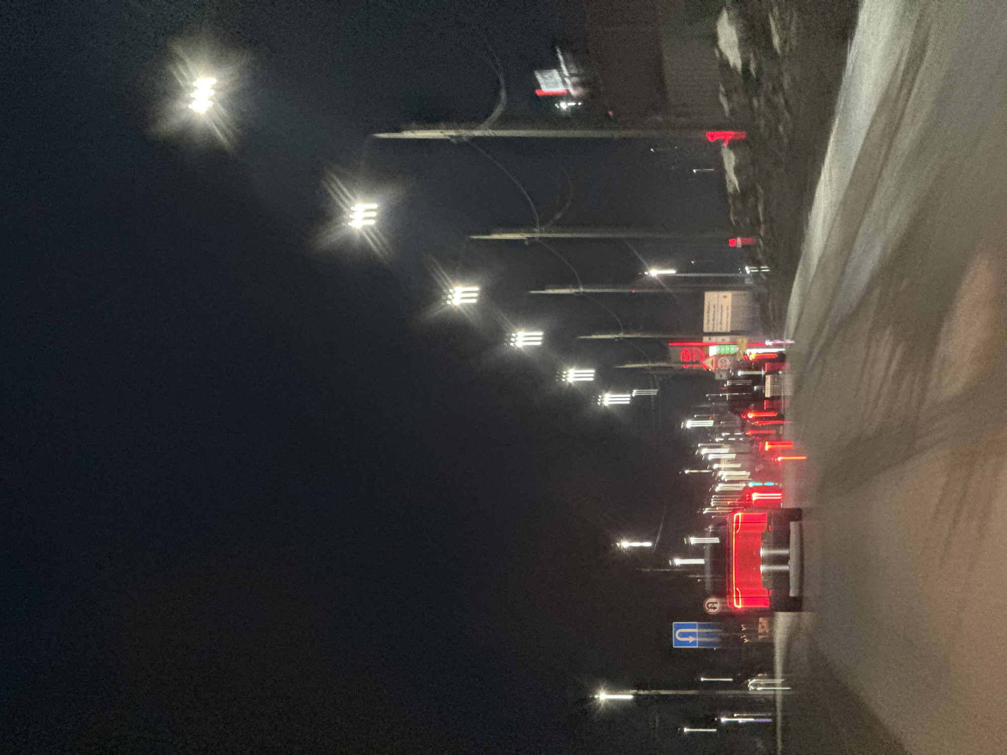 The image shows a night scene of a road in Chaikovsky, Russia. Streetlights line the road, and there are visible red and white lights from vehicles and buildings. The road surface appears wet or icy. There are road signs present. The overall environment is dark and suggestive of a cold climate.